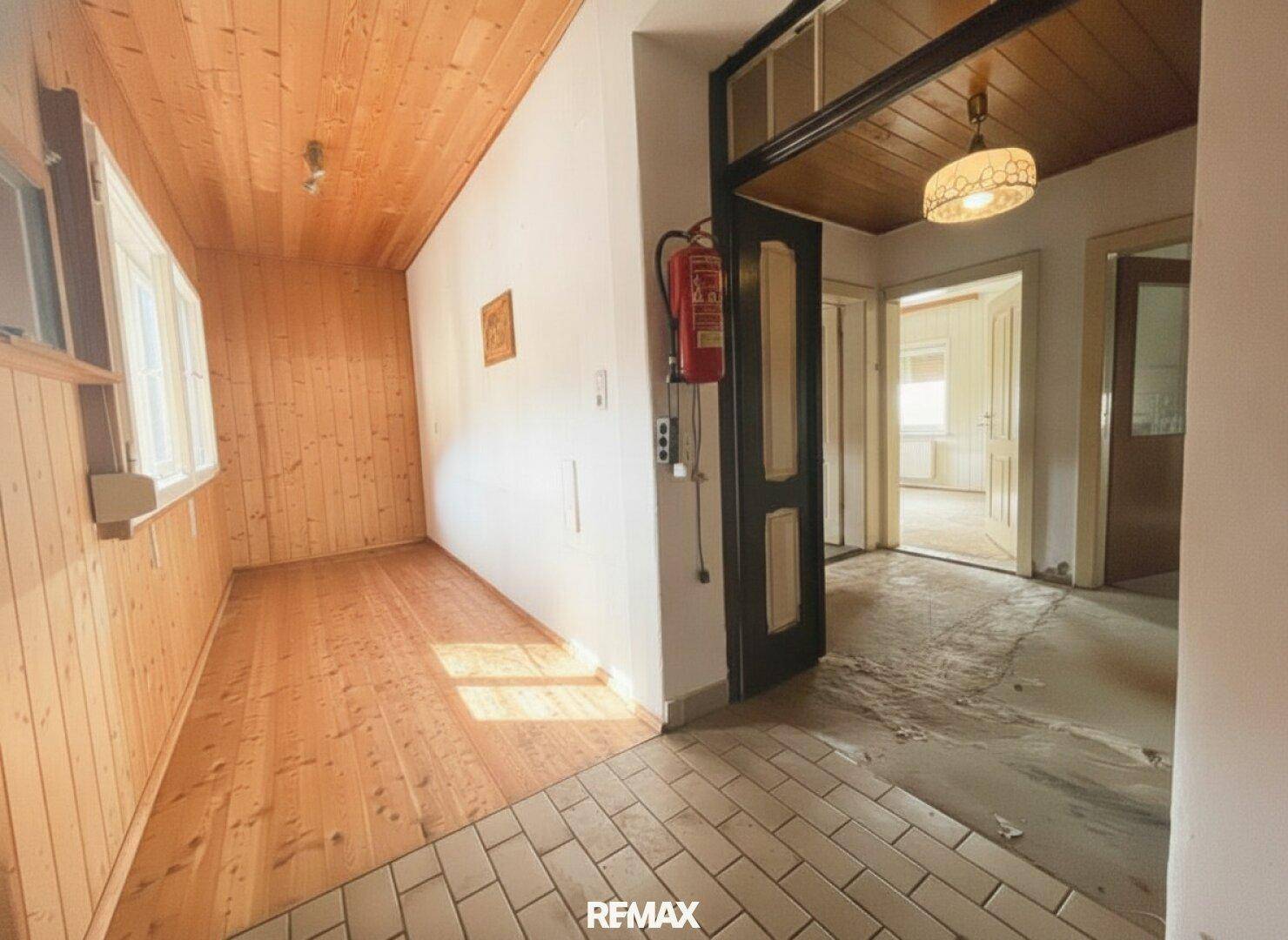 Eingangsbereich mit Holzwänden, Holzboden und Fliesen, der zu weiteren Räumen führt.