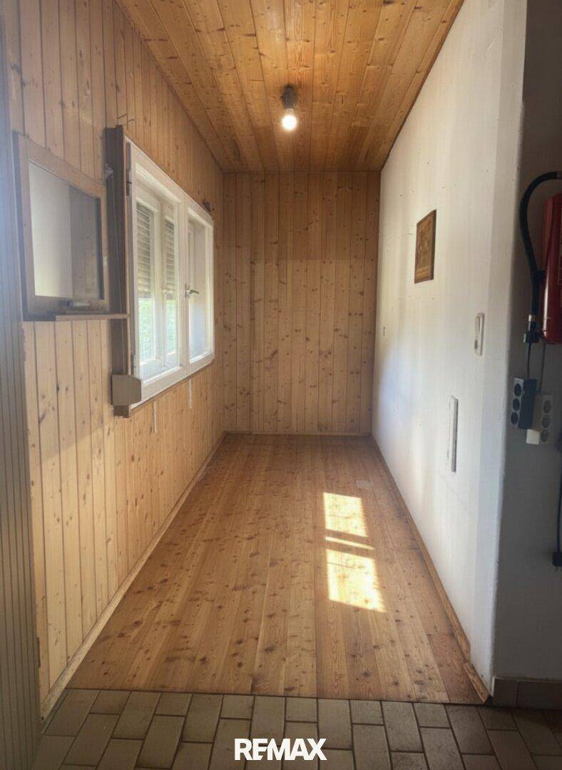 Heller Flur mit Holzdielenboden und Holzwänden, der den Übergang zu einem gefliesten Bereich zeigt.