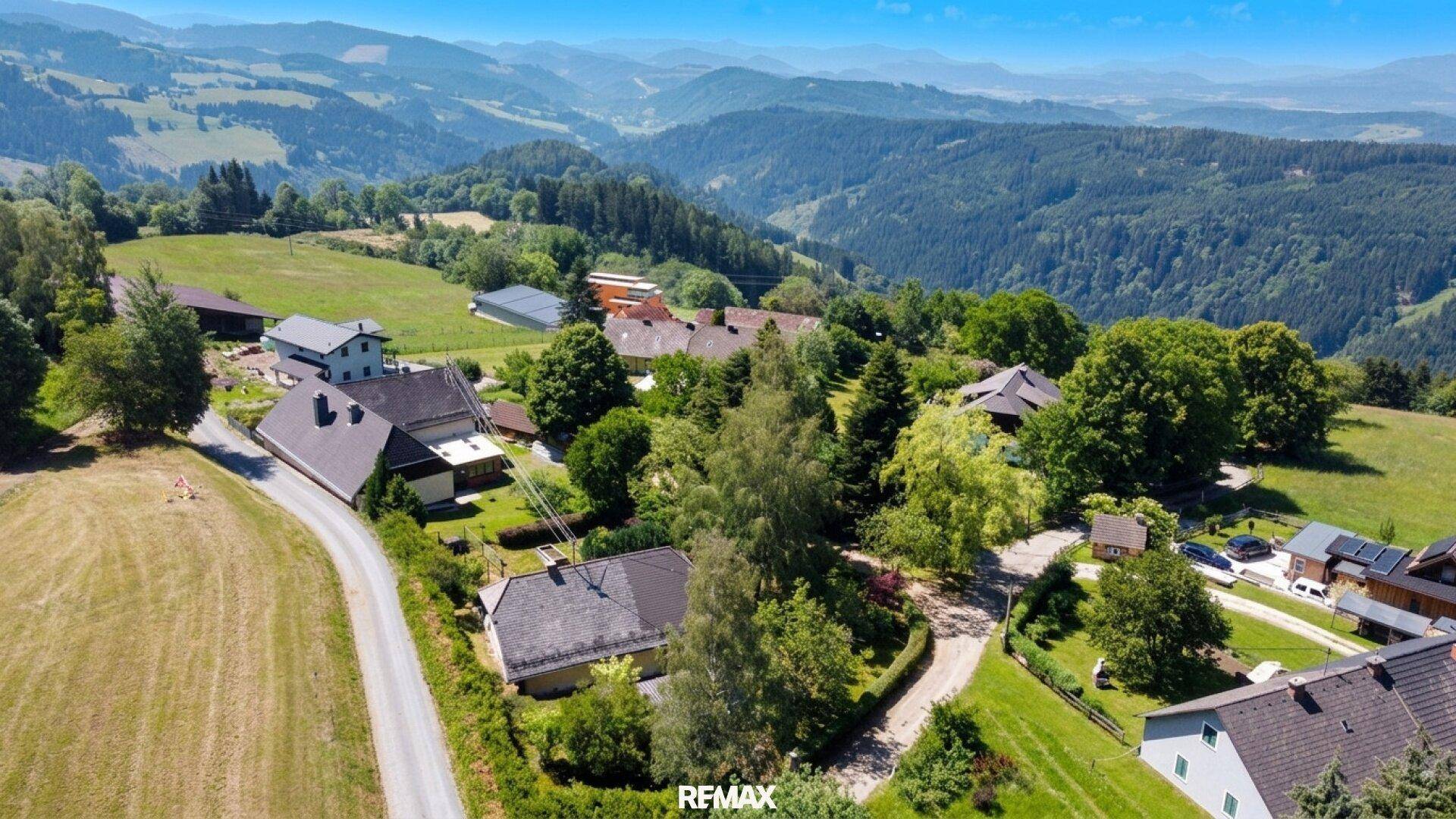 Weitläufige Ansicht mehrerer Häuser in einer idyllischen Berglandschaft mit viel Grün.
