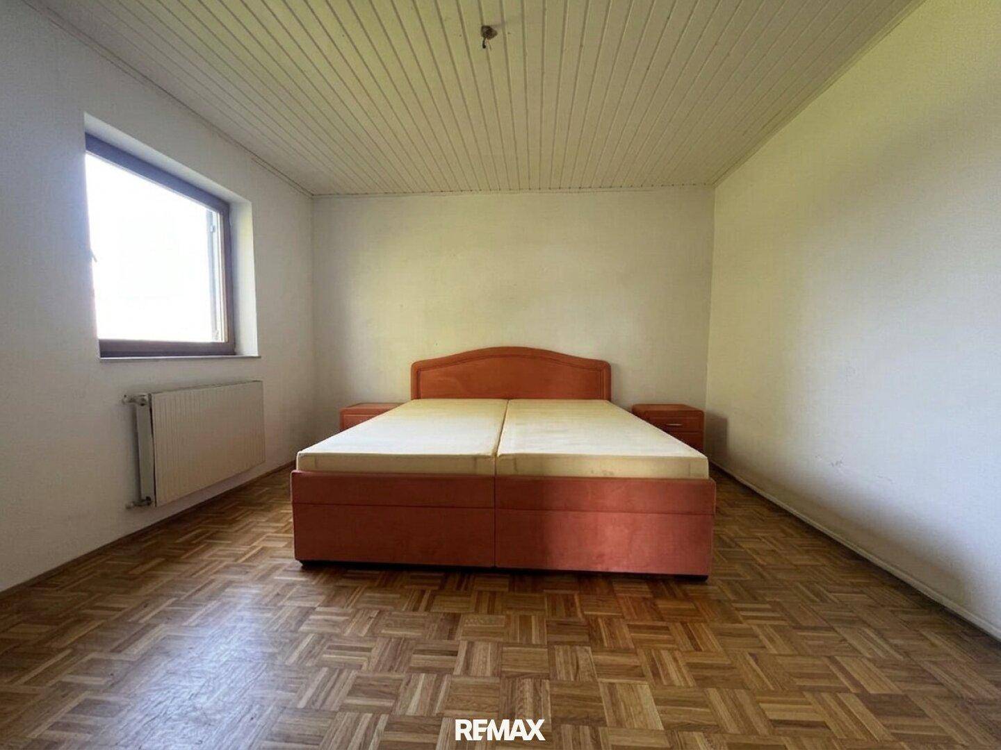 Helles Schlafzimmer mit Holzbalkendecke, Parkettboden und einem großen Fenster.
