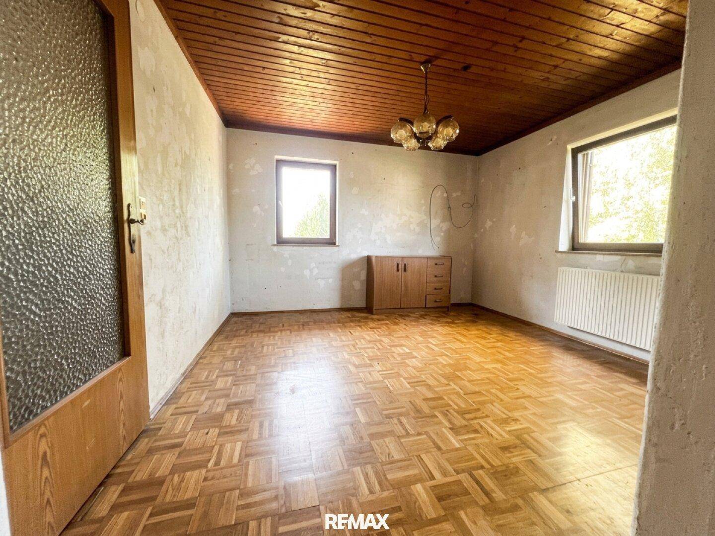Leerer Raum mit Holzbalkendecke, Parkettboden und zwei Fenstern für natürliches Licht.