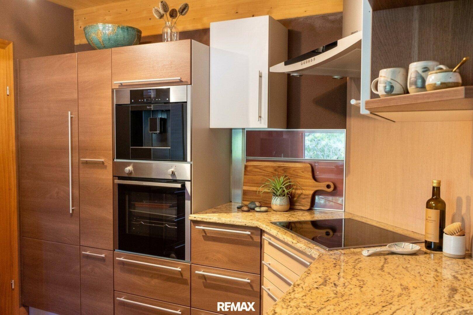 Moderne Küche mit Holzelementen, Granitarbeitsplatte und hochwertigen Einbaugeräten.