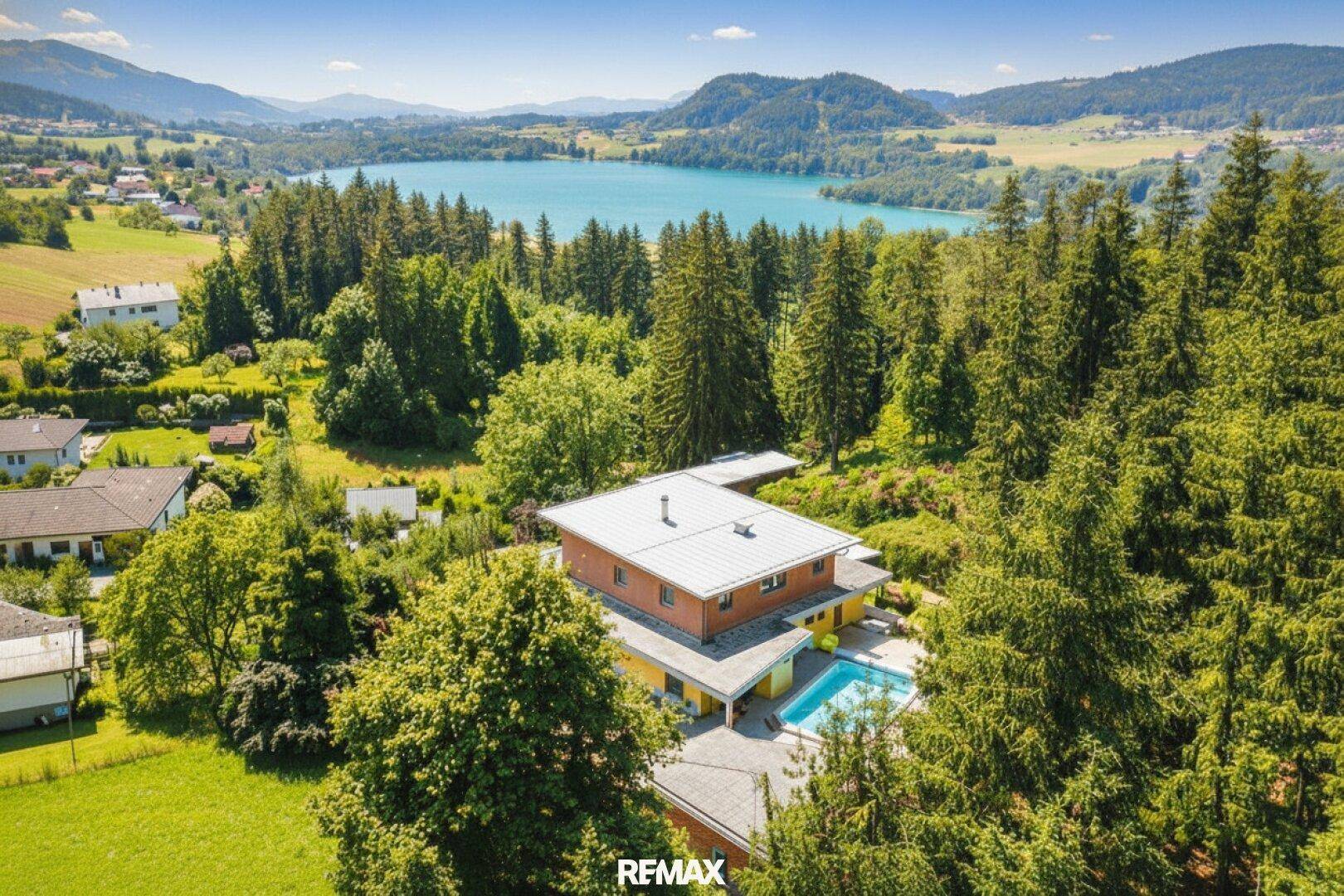 Luftaufnahme eines Anwesens mit Haus, Pool und weitem Blick auf einen See und die umliegende Landschaft.