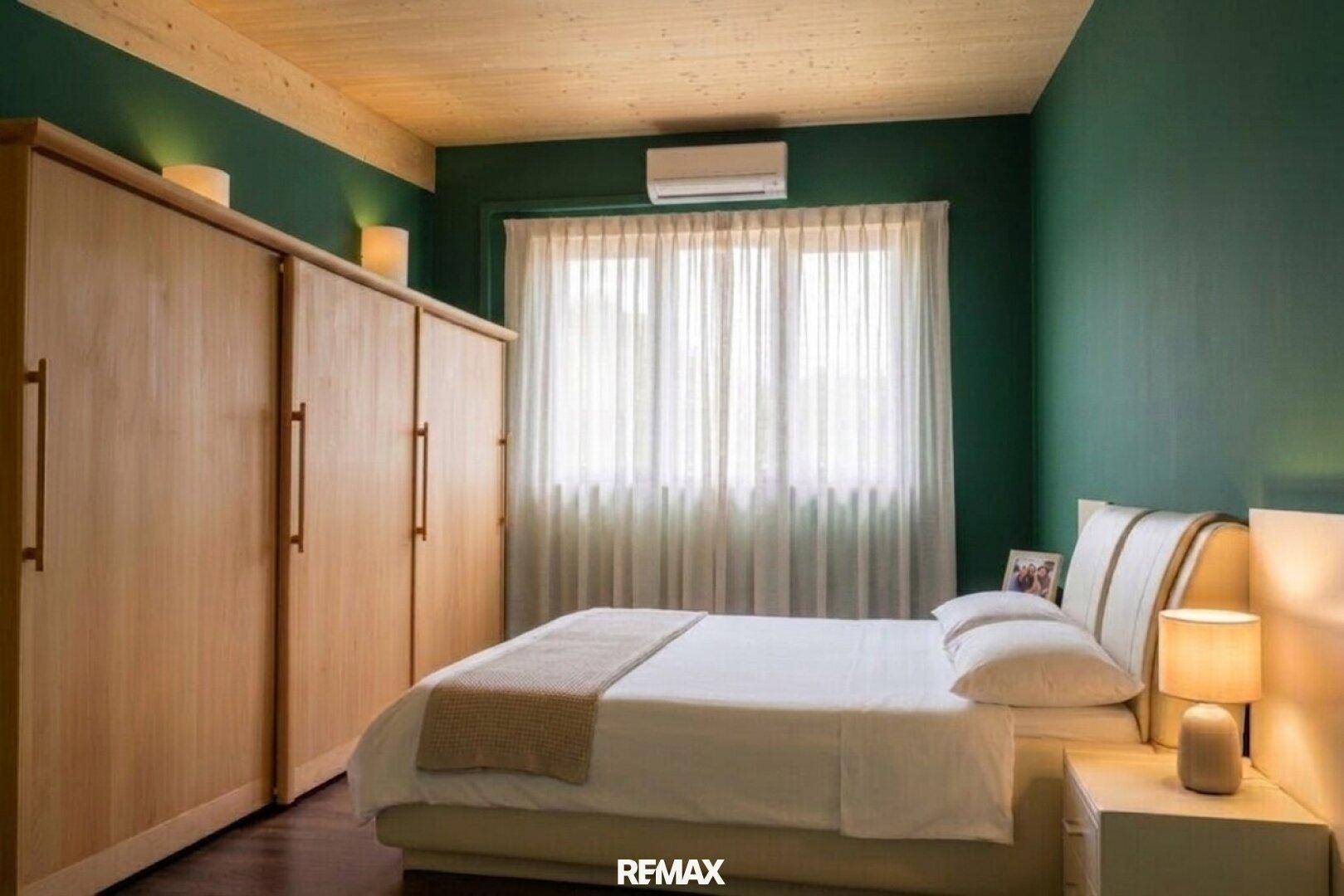 Schlafzimmer mit großem Bett, Holzschrank, Klimaanlage und grünen Wänden.