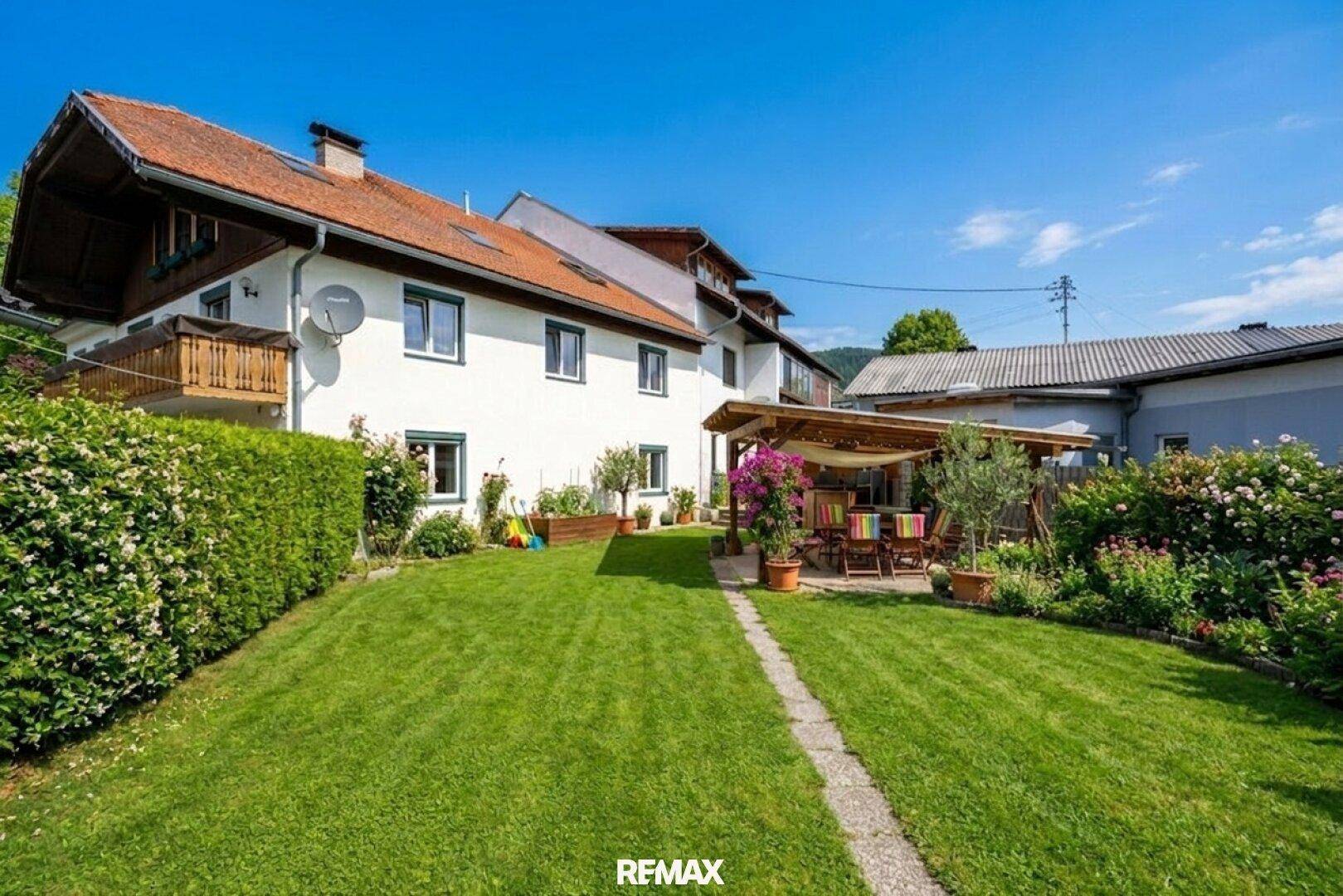 Gepflegter Garten mit Rasenfläche, Hecke und überdachtem Sitzbereich.