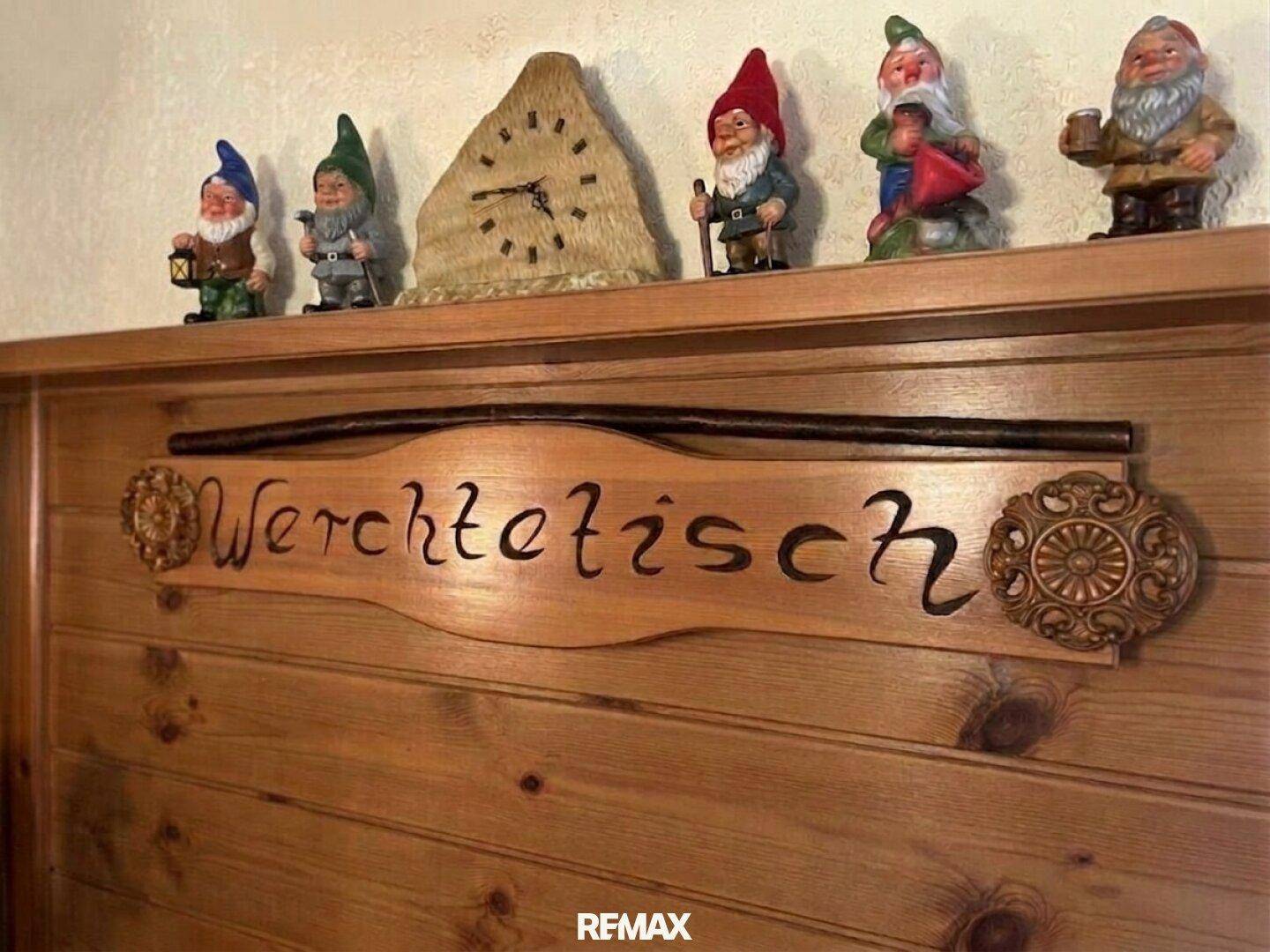 Detailaufnahme einer Holzwanddekoration mit geschnitztem Schriftzug und Gartenzwergen auf einem Regal.