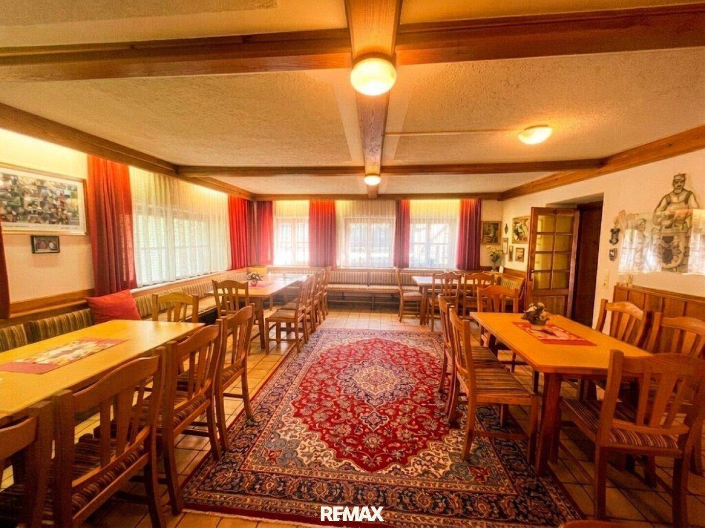 Großer Speisesaal mit vielen Holztischen, Stühlen und einem gemusterten Teppichboden.