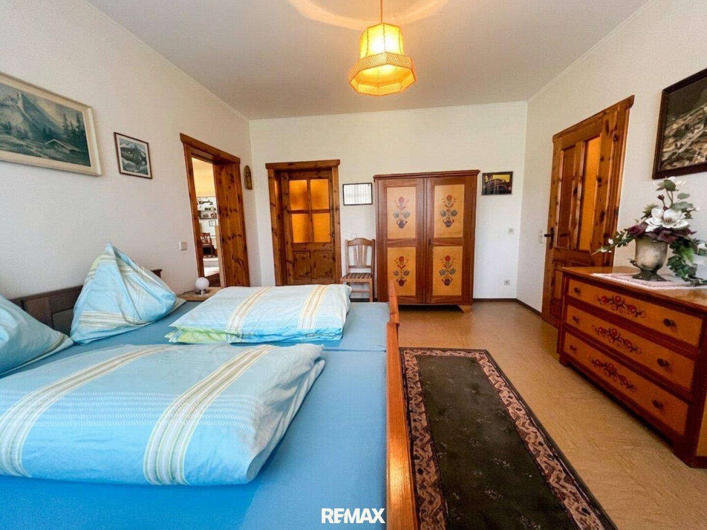 Schlafzimmer mit Holzrahmenbett, blauer Bettwäsche und traditionellen bemalten Möbeln.