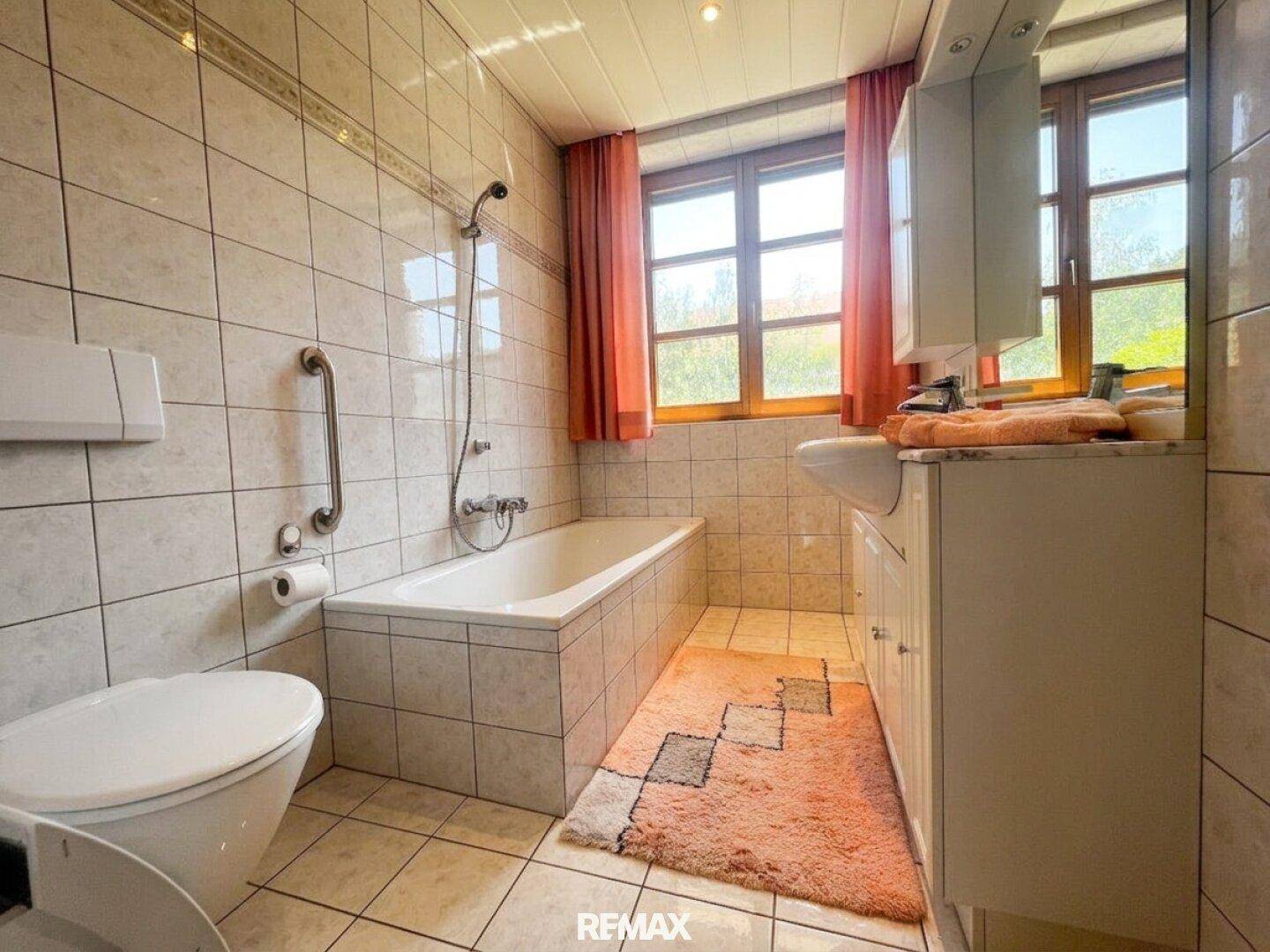 Gefliestes Badezimmer mit Badewanne, Dusche, Toilette und Waschtisch, ausgestattet mit Haltegriffen.