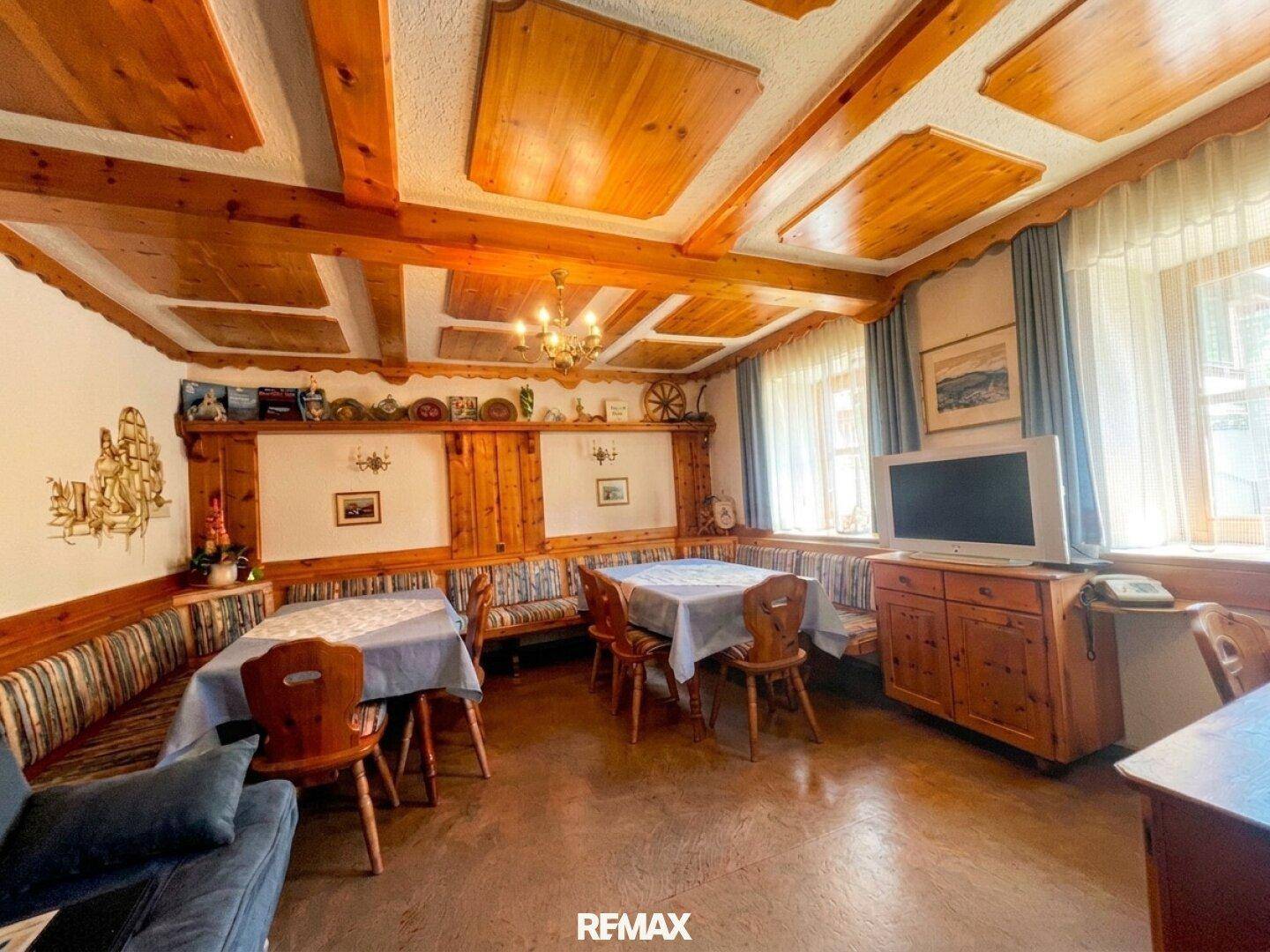 Rustikaler Essbereich mit Holztischen, Bänken und traditioneller Holzvertäfelung an Wänden und Decke.