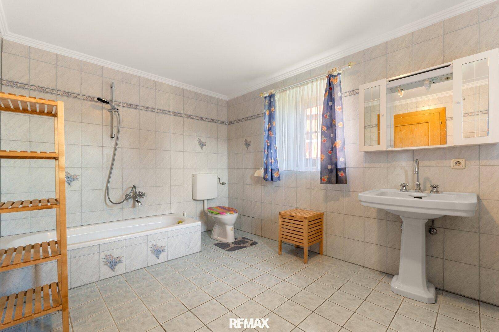 Geräumiges Badezimmer mit hellen Fliesen, Badewanne, WC und Fenster für Tageslicht.