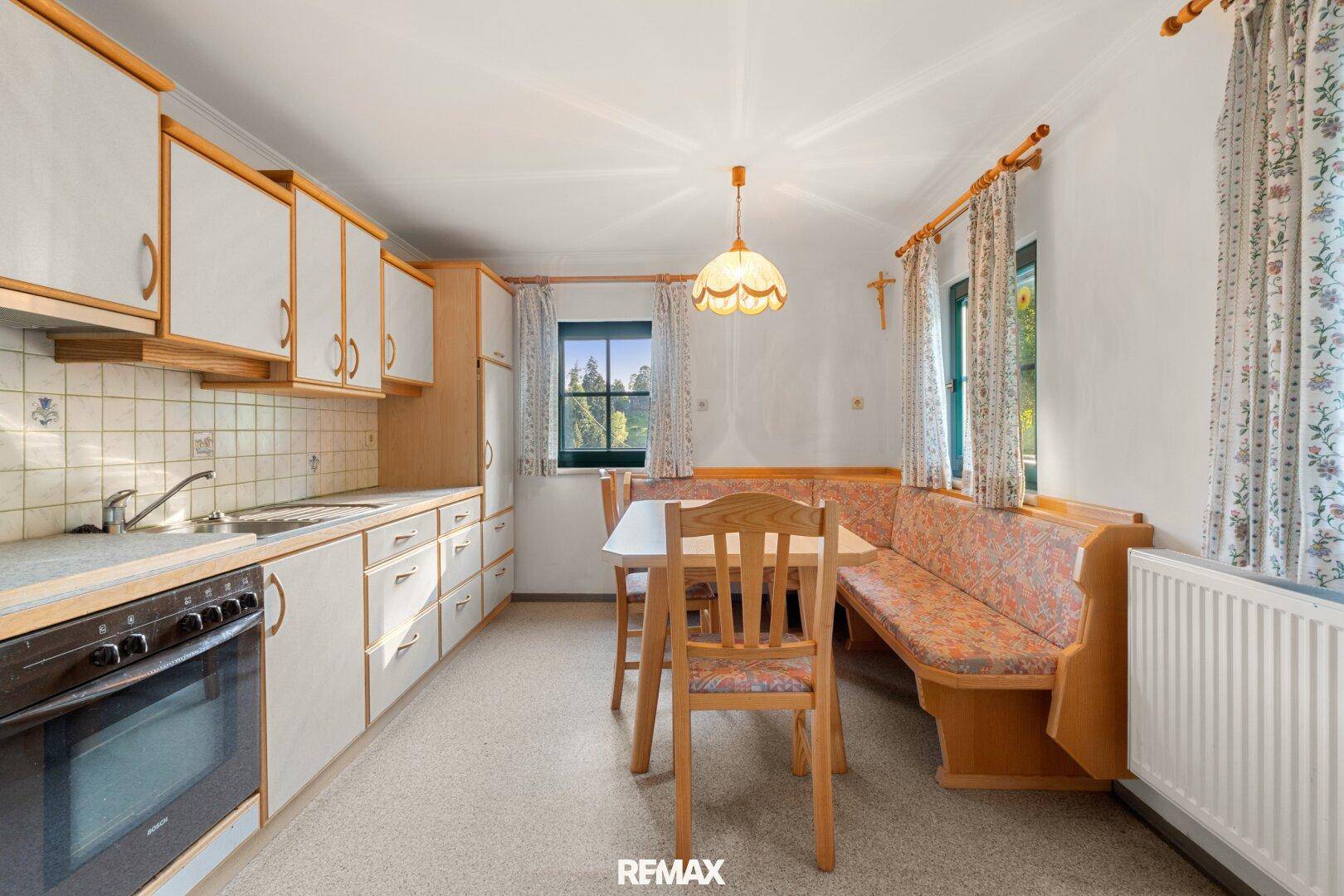 Gemütliche Wohnküche mit Holzeinbauten, Essbereich und Blick ins Grüne durch das Fenster.