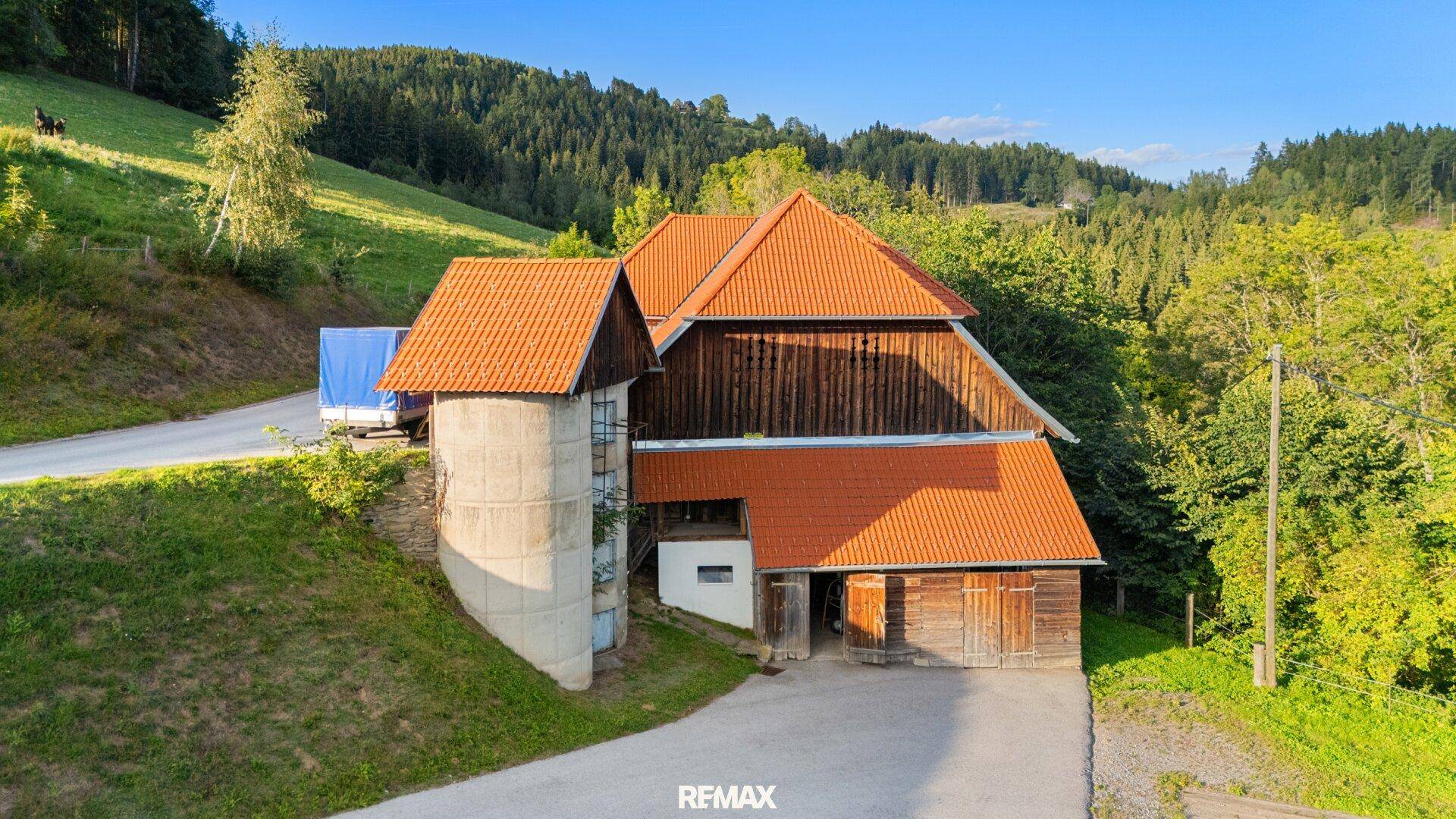 Großes traditionelles Bauernhaus mit Silo, roten Ziegeldächern und Holzfassade in ländlicher Umgebung.