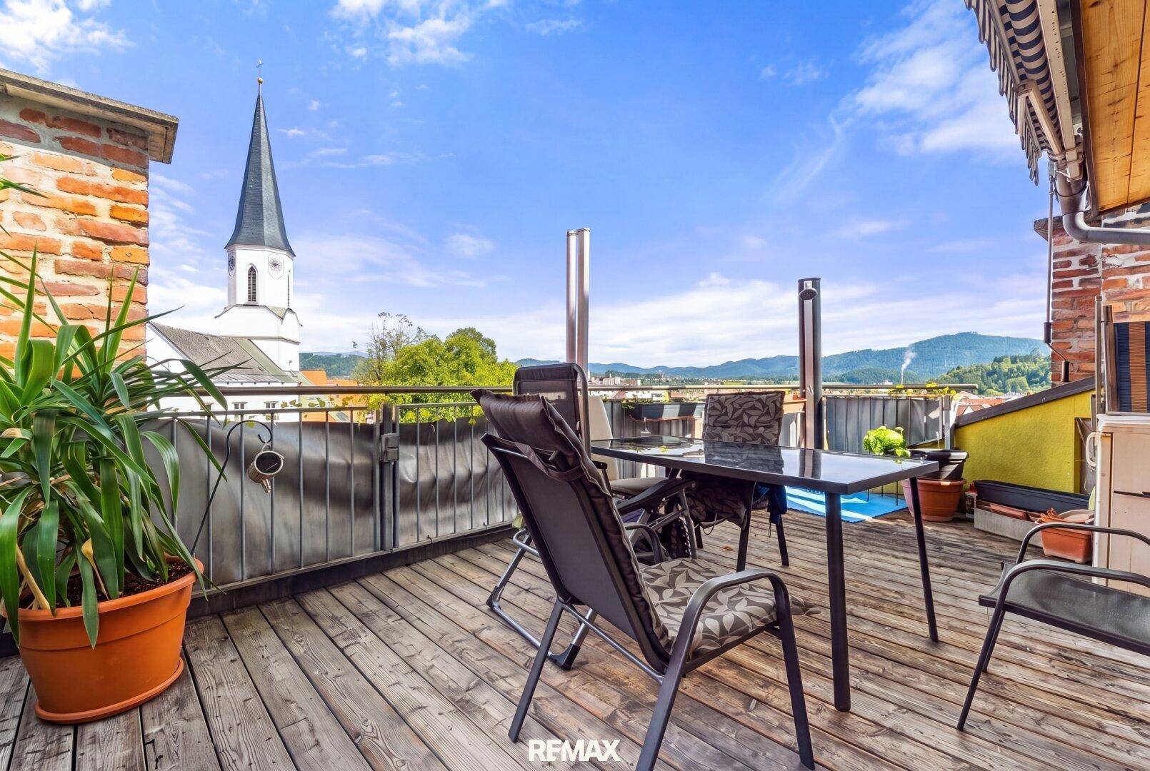 Große Dachterrasse mit Holzboden, Gartenmöbeln und weitem Blick über die Stadt und Berge.