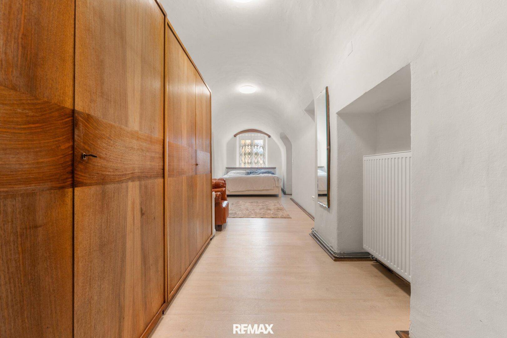 Langer Flur mit Holzeinbauschränken und gewölbter Decke, der zu einem Schlafzimmer führt.