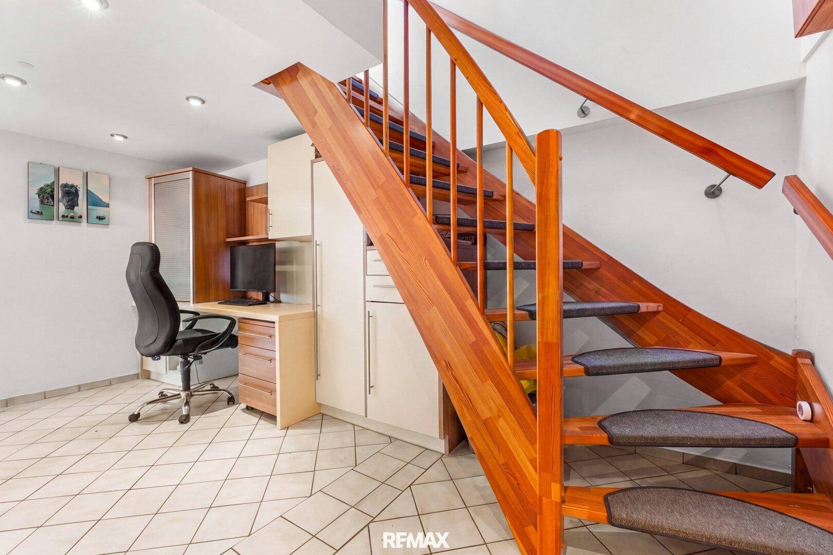 Kleiner Arbeitsbereich unter einer Holztreppe mit Schreibtisch und Stauraum.