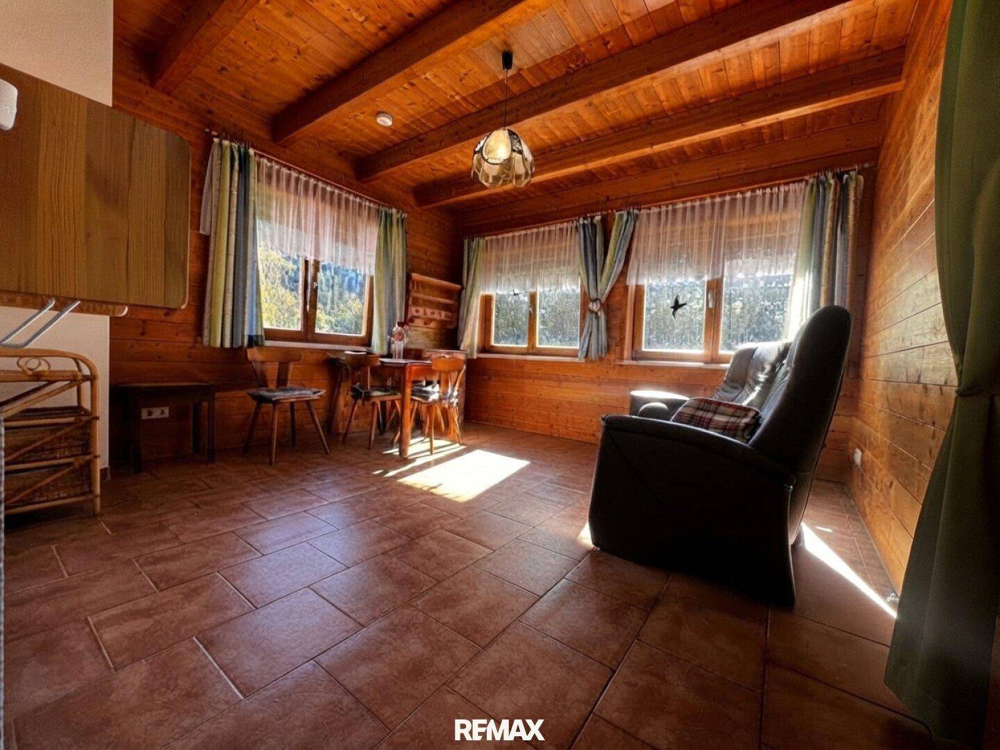 Gemütliches Wohnzimmer im alpinen Stil mit Holzbalkendecke und Fliesenboden.