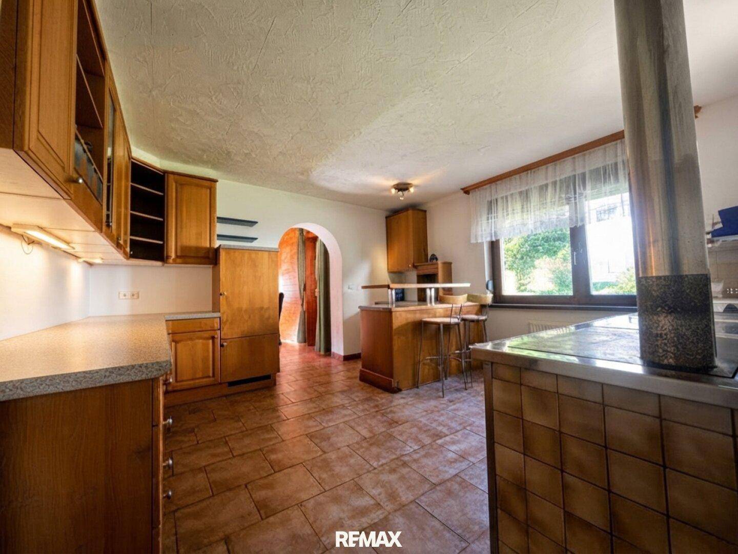 Geräumige Küche mit Holzschränken, Fliesenboden und einem Durchgang zu weiteren Räumen.