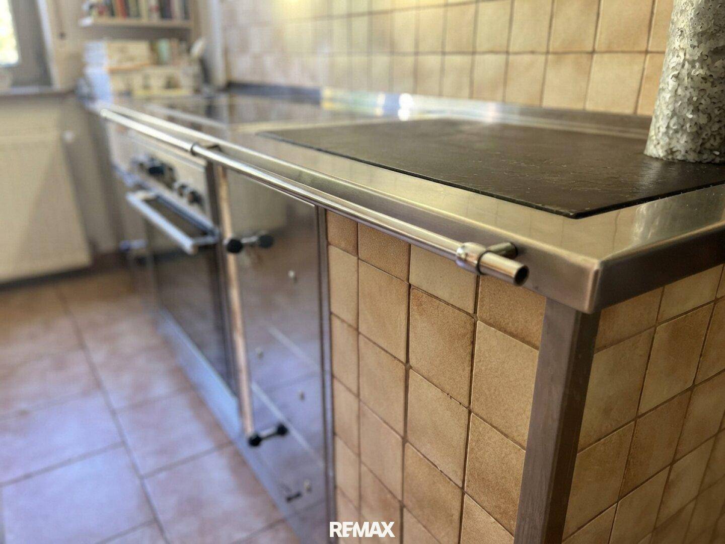 Detailansicht des Herdbereichs in der Küche mit Edelstahl-Arbeitsfläche und Fliesen.