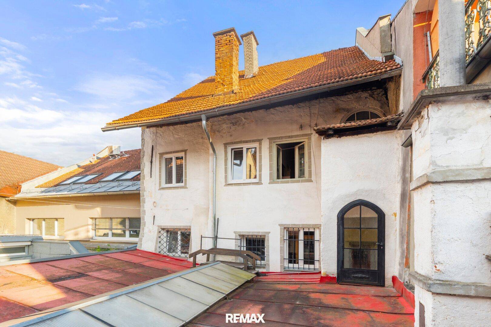 Ansicht eines historischen Gebäudes mit weißer Fassade, rotem Ziegeldach und kleinen Fenstern von oben.