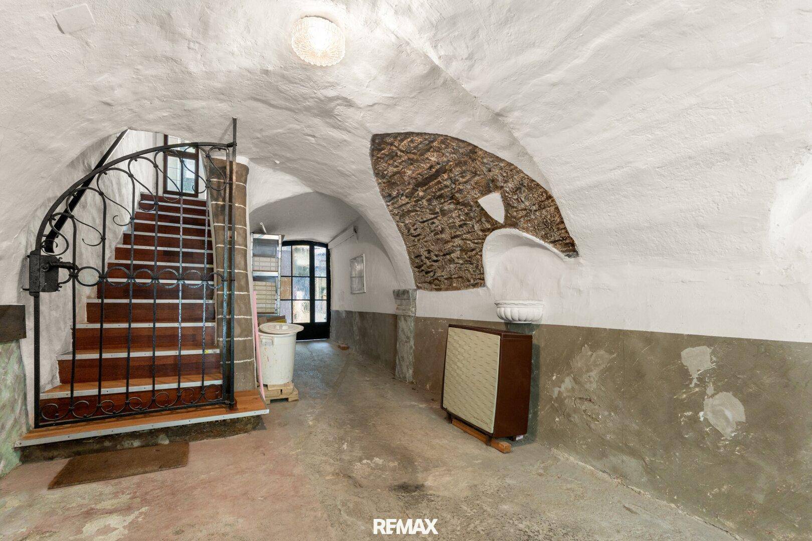 Historischer Kellergang mit Gewölbedecke und schmiedeeisernem Tor, das zu einer Treppe führt.
