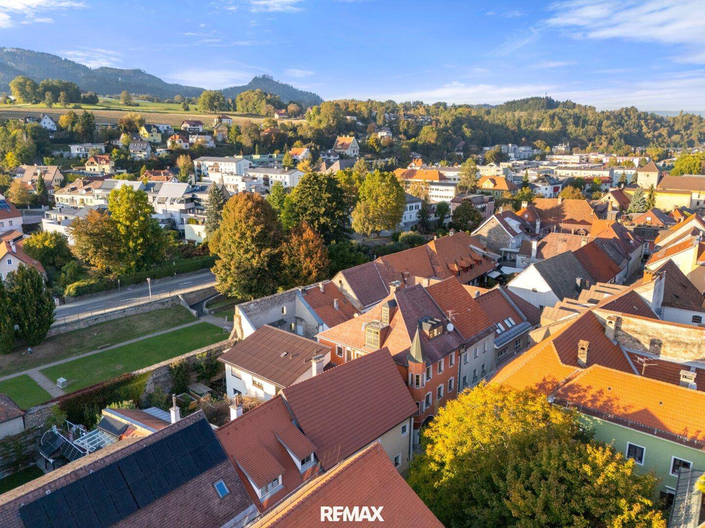 Weitläufige Luftaufnahme der historischen Stadt mit ihren Dächern und der malerischen grünen Hügellandschaft.