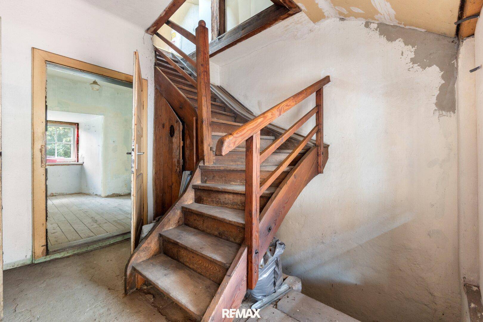 Rustikale Holztreppe in einem alten Gebäude mit abgenutzten Wänden, die auf eine Renovierung wartet.