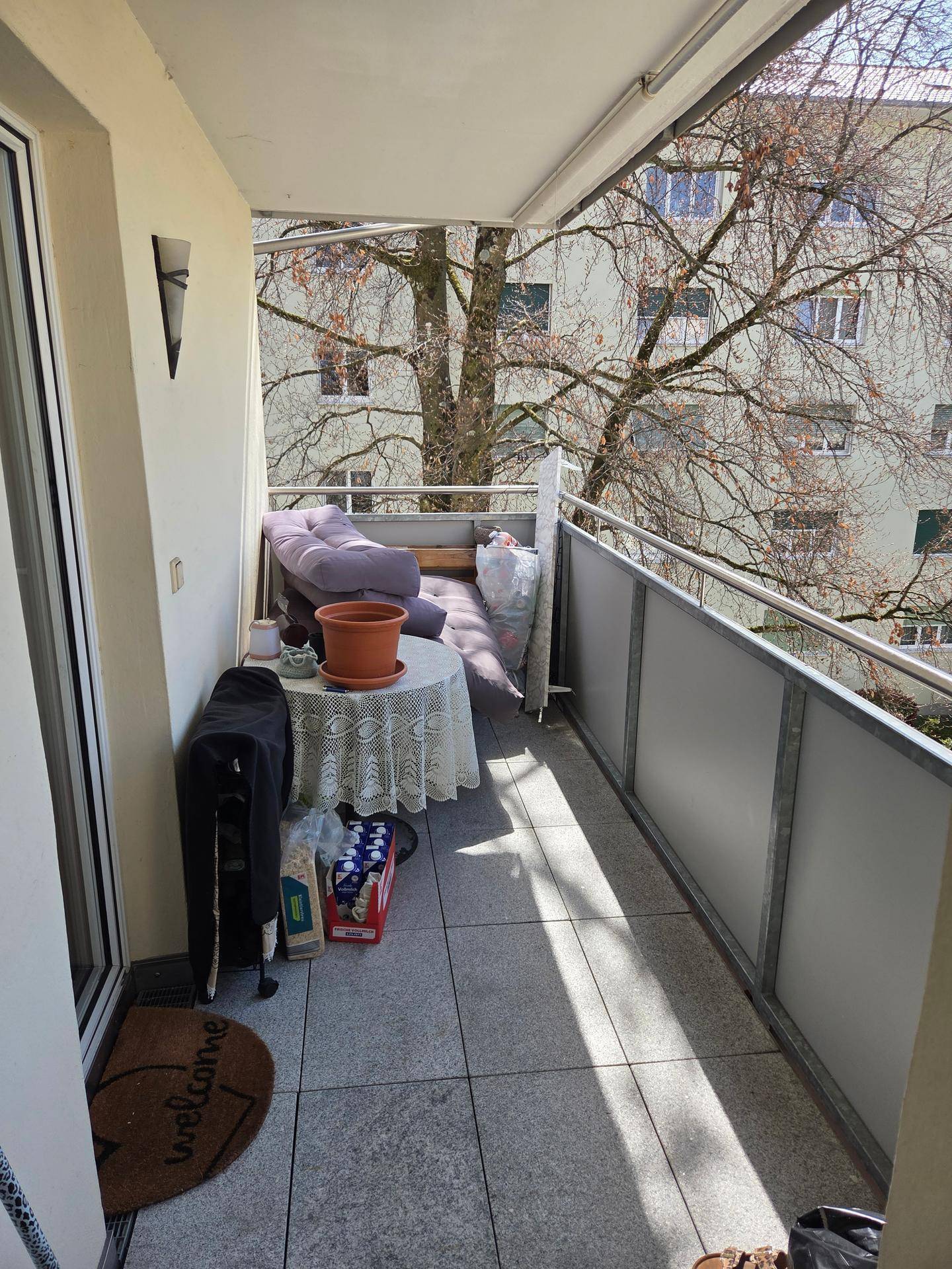 Balkon mit Fliesenboden, Metallgeländer und Blick auf Bäume.