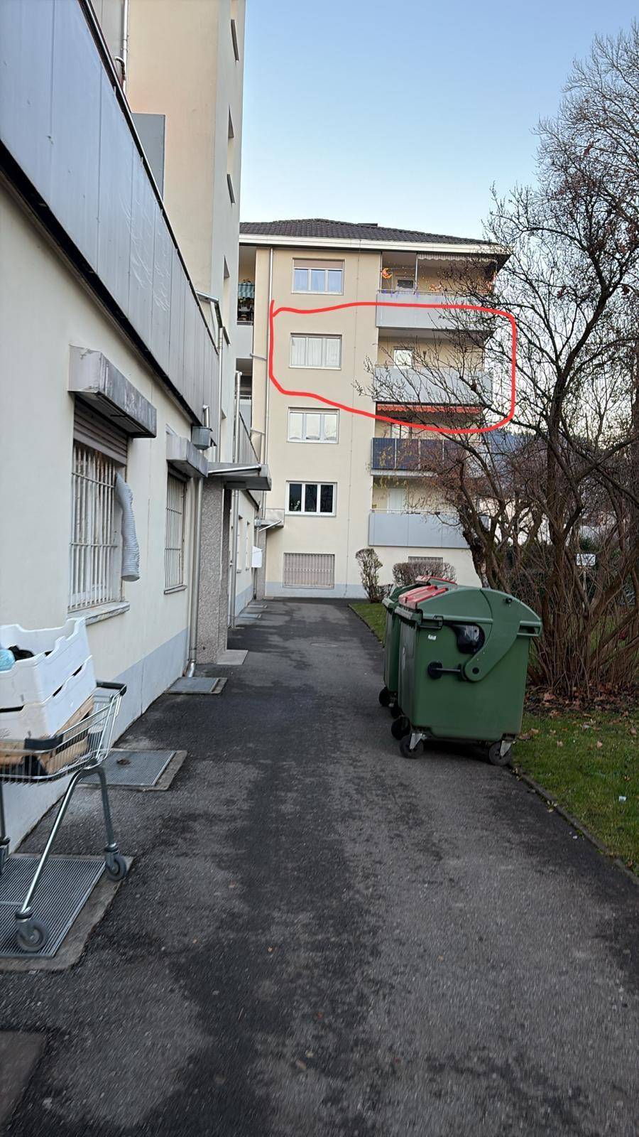 Außenansicht eines Mehrfamilienhauses mit Balkonen und Mülltonnen im Vordergrund.
