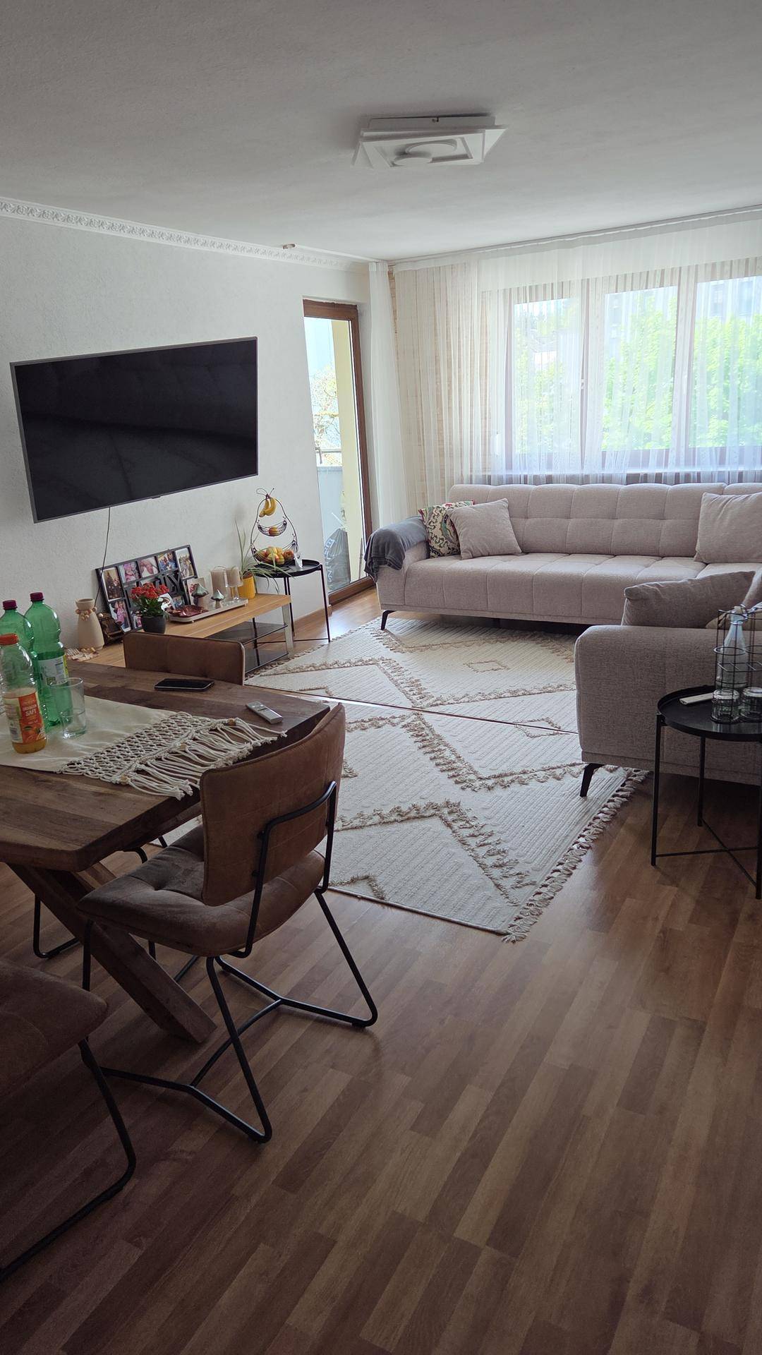 Geräumiger Wohn- und Essbereich mit Holzboden, großem Sofa und Zugang zum Balkon.