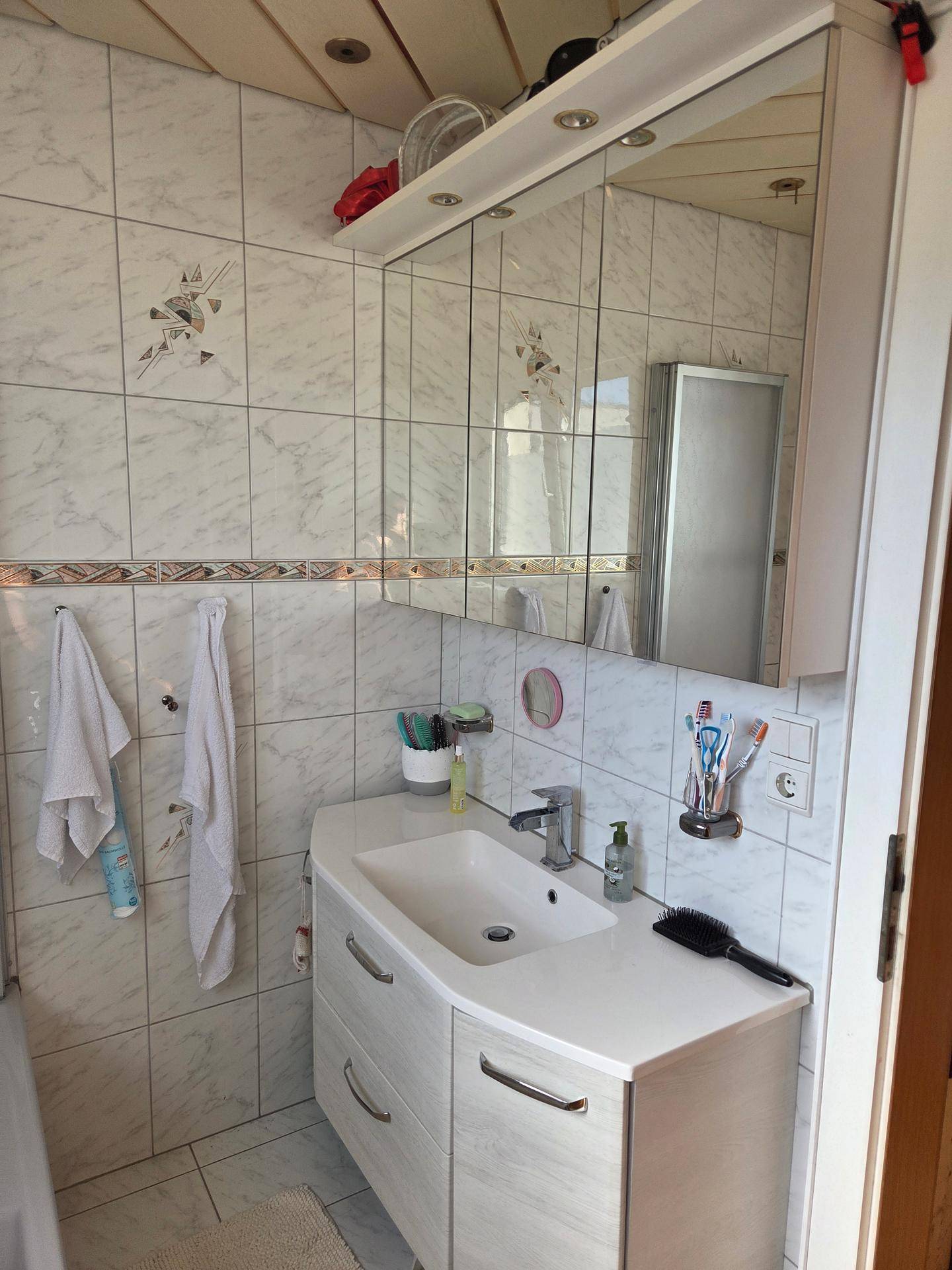 Helles Badezimmer mit Waschtisch, Spiegelschrank und Duschkabine.