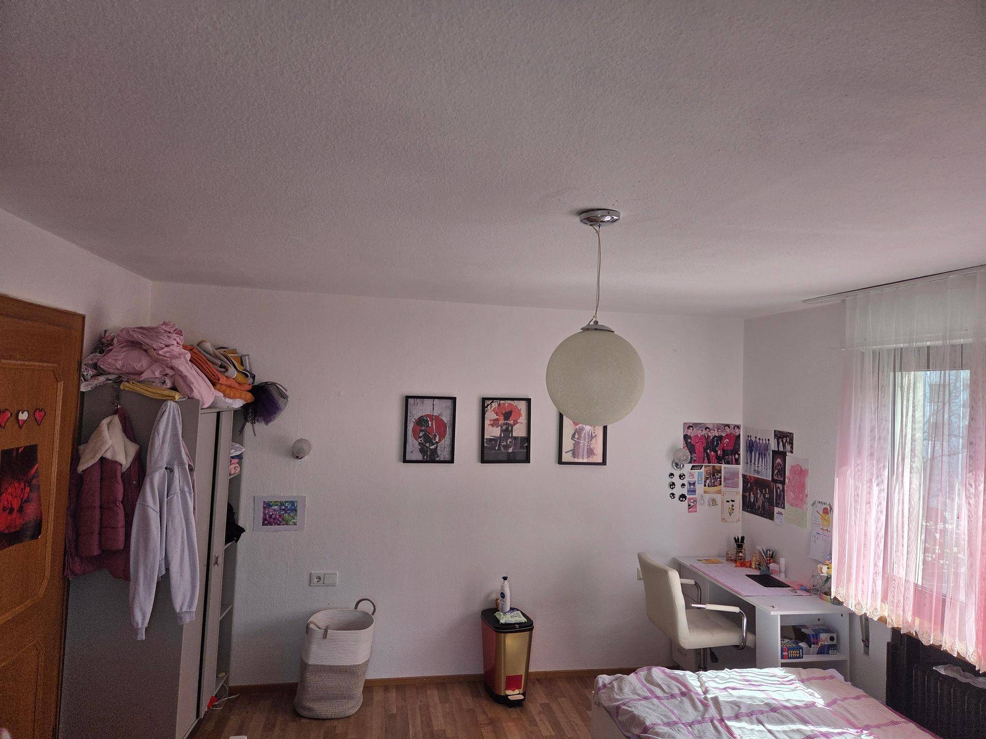 Helles Schlafzimmer mit Schreibtisch, Kleiderschrank und Fenster.