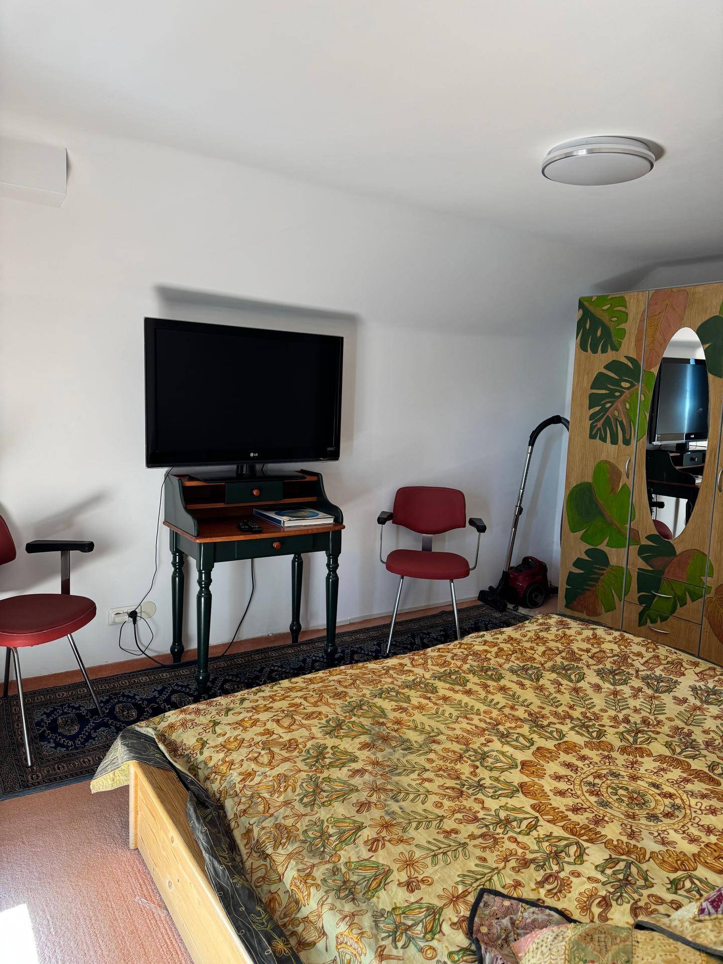 Schlafzimmer mit Fernseher, Kleiderschrank und farbenfroher Bettwäsche in einem gemütlichen Ambiente.