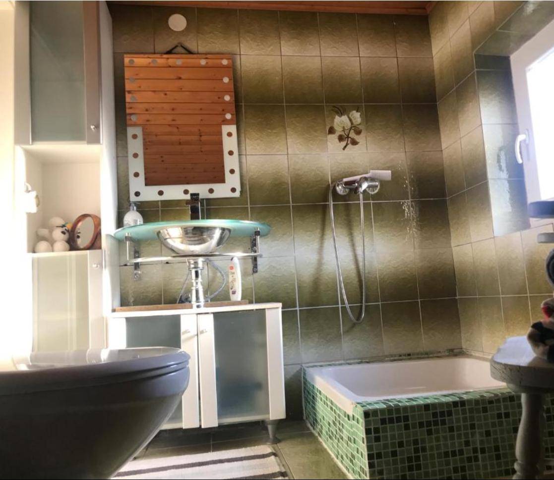 Badezimmer mit grünen Fliesen, kleiner Badewanne und modernem Waschbecken.