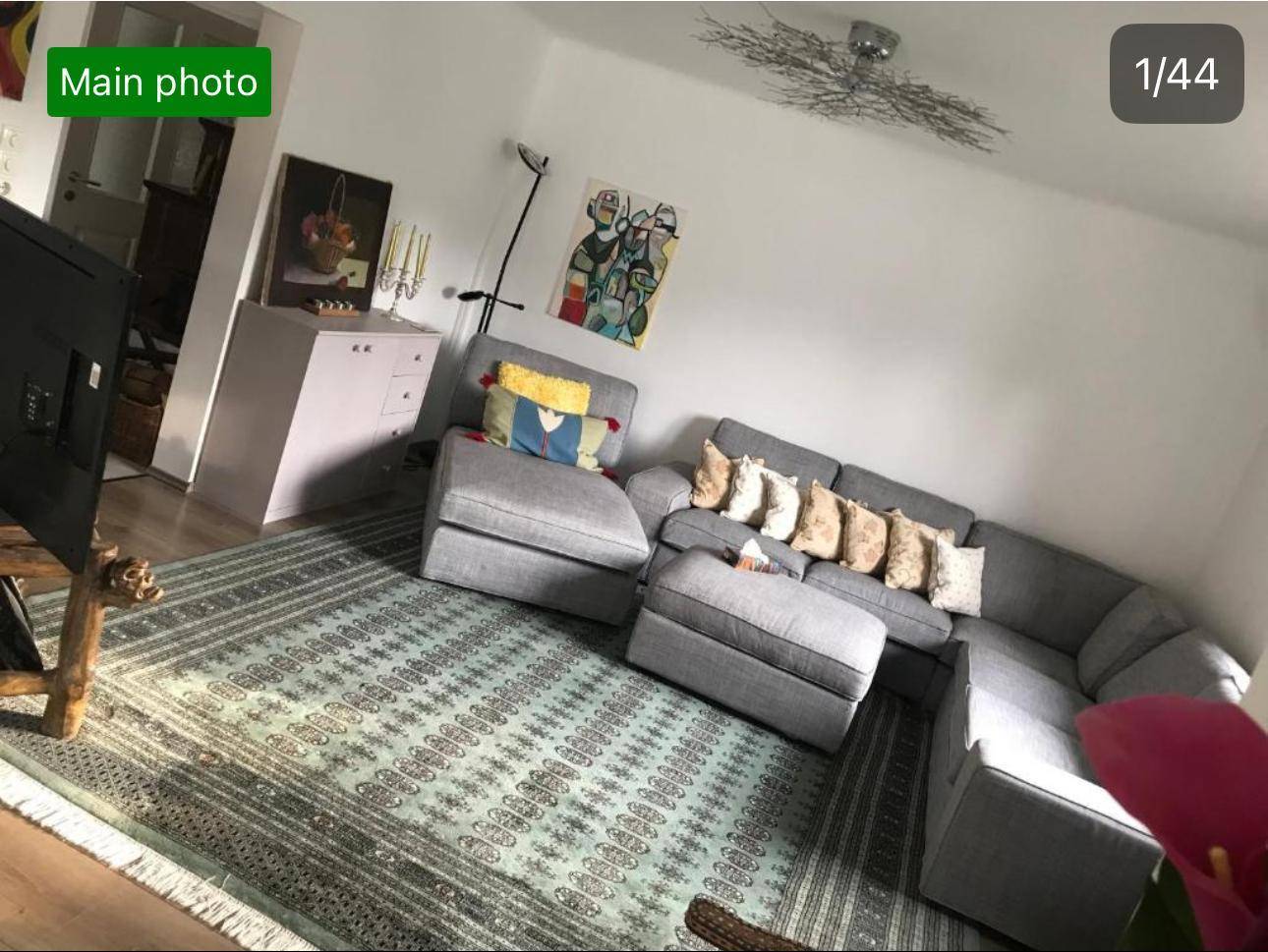 Helles Wohnzimmer mit bequemer grauer Sofalandschaft, Teppich und moderner Dekoration.