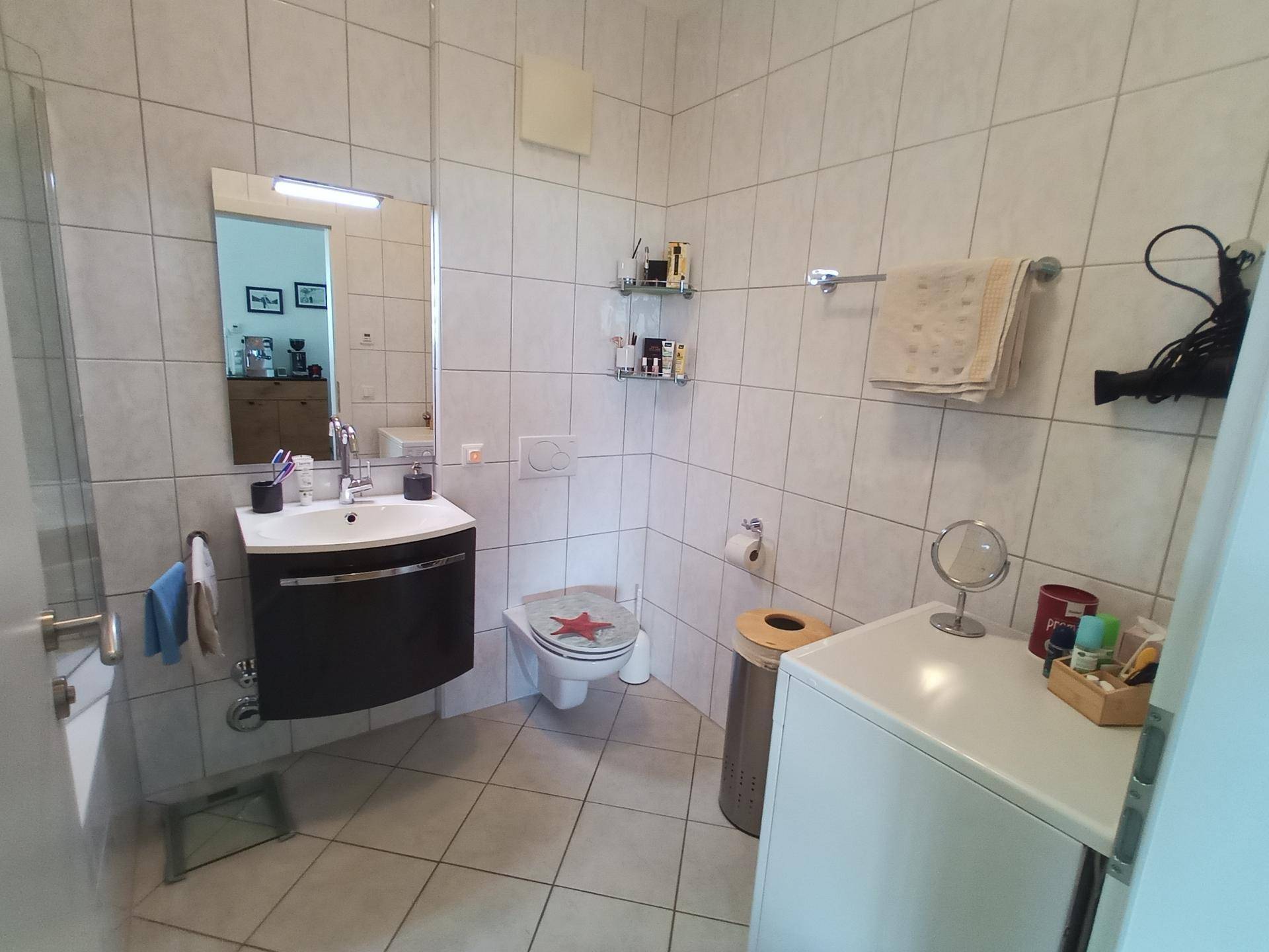 Gefliestes Badezimmer mit WC, Waschbecken und Waschmaschine.