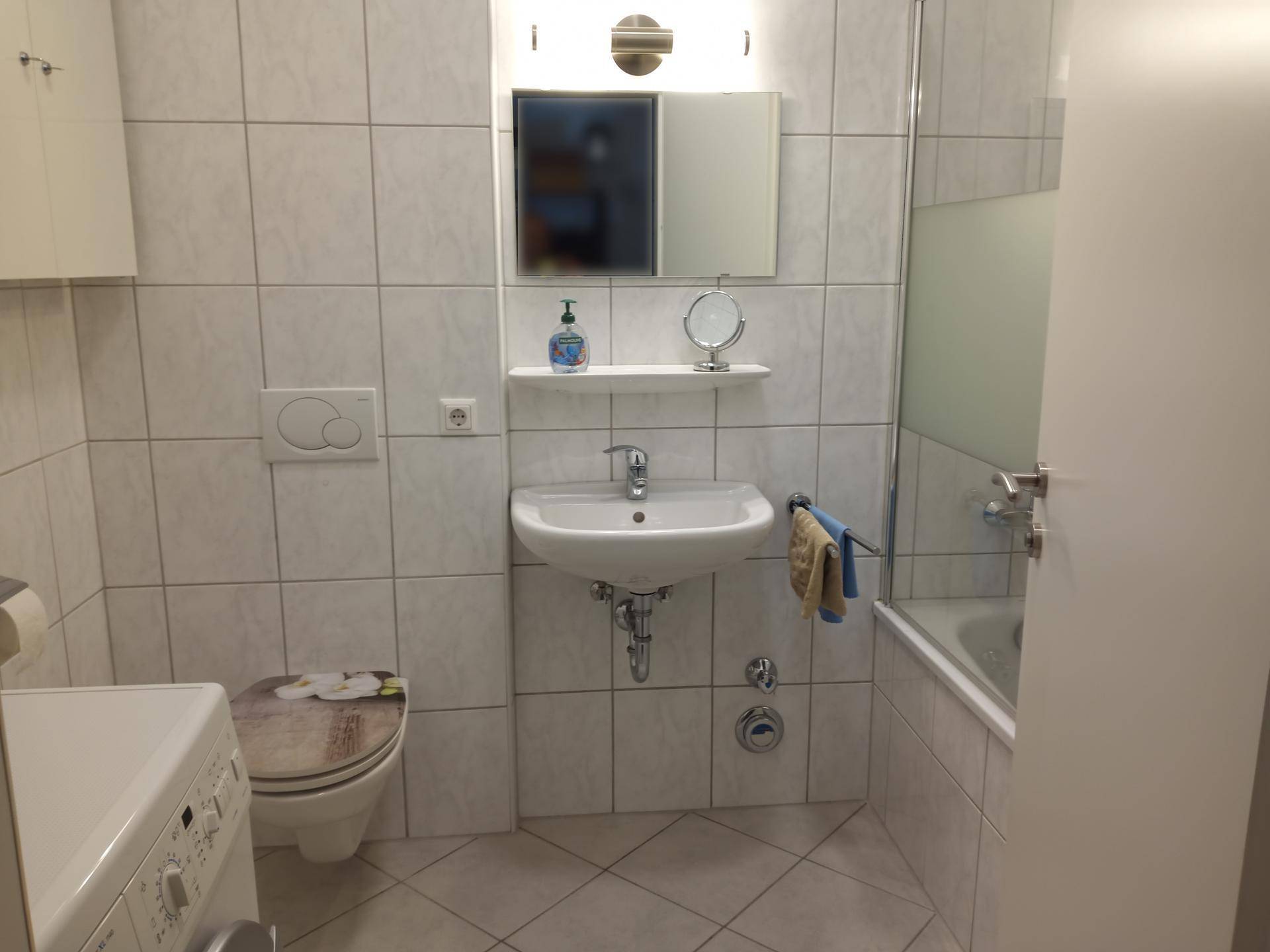 Gefliestes Badezimmer mit WC, Waschbecken und Badewanne mit Duschfunktion.