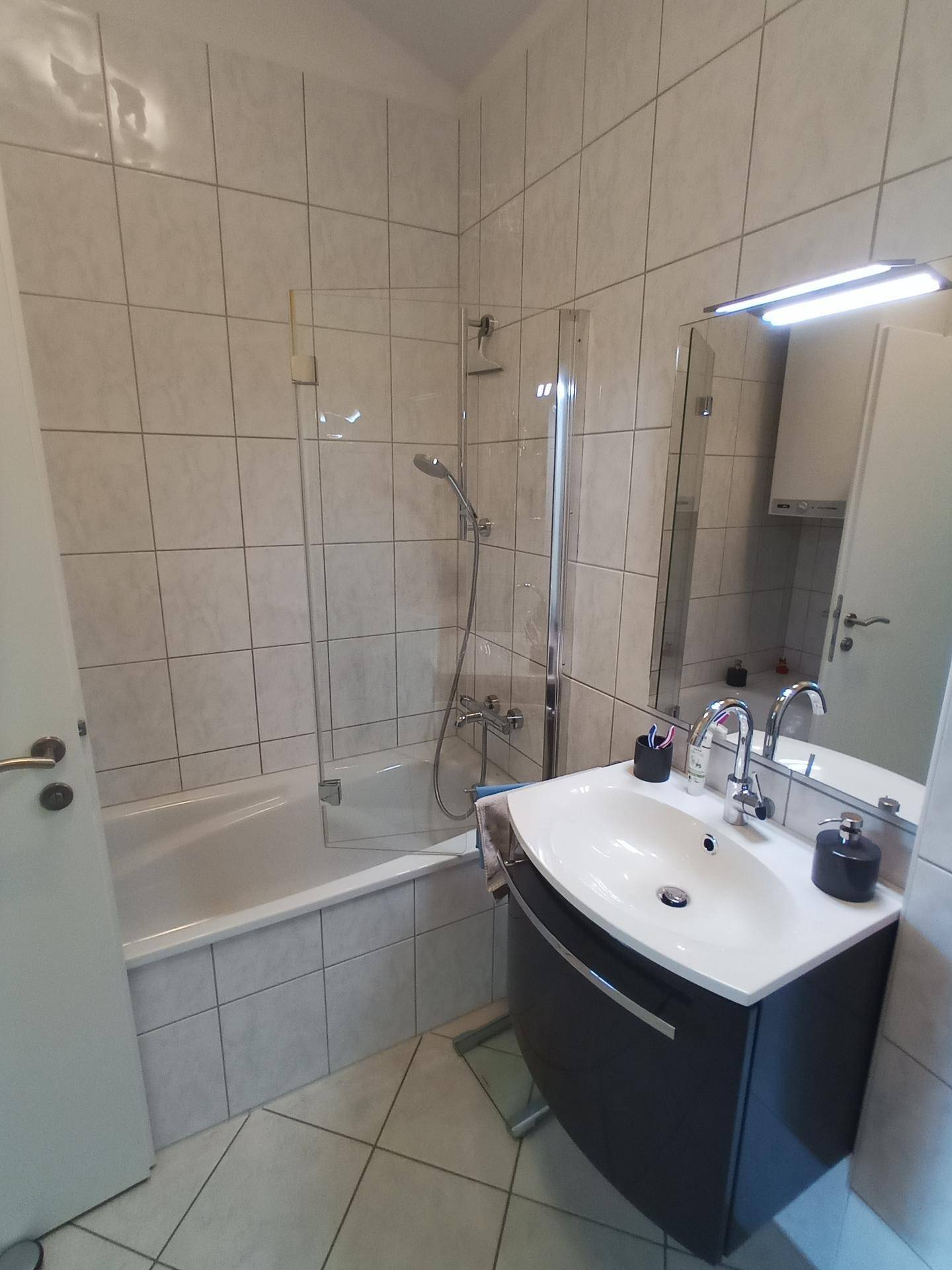 Badezimmer mit Badewanne, Duschwand, Waschbecken und Fliesenboden.