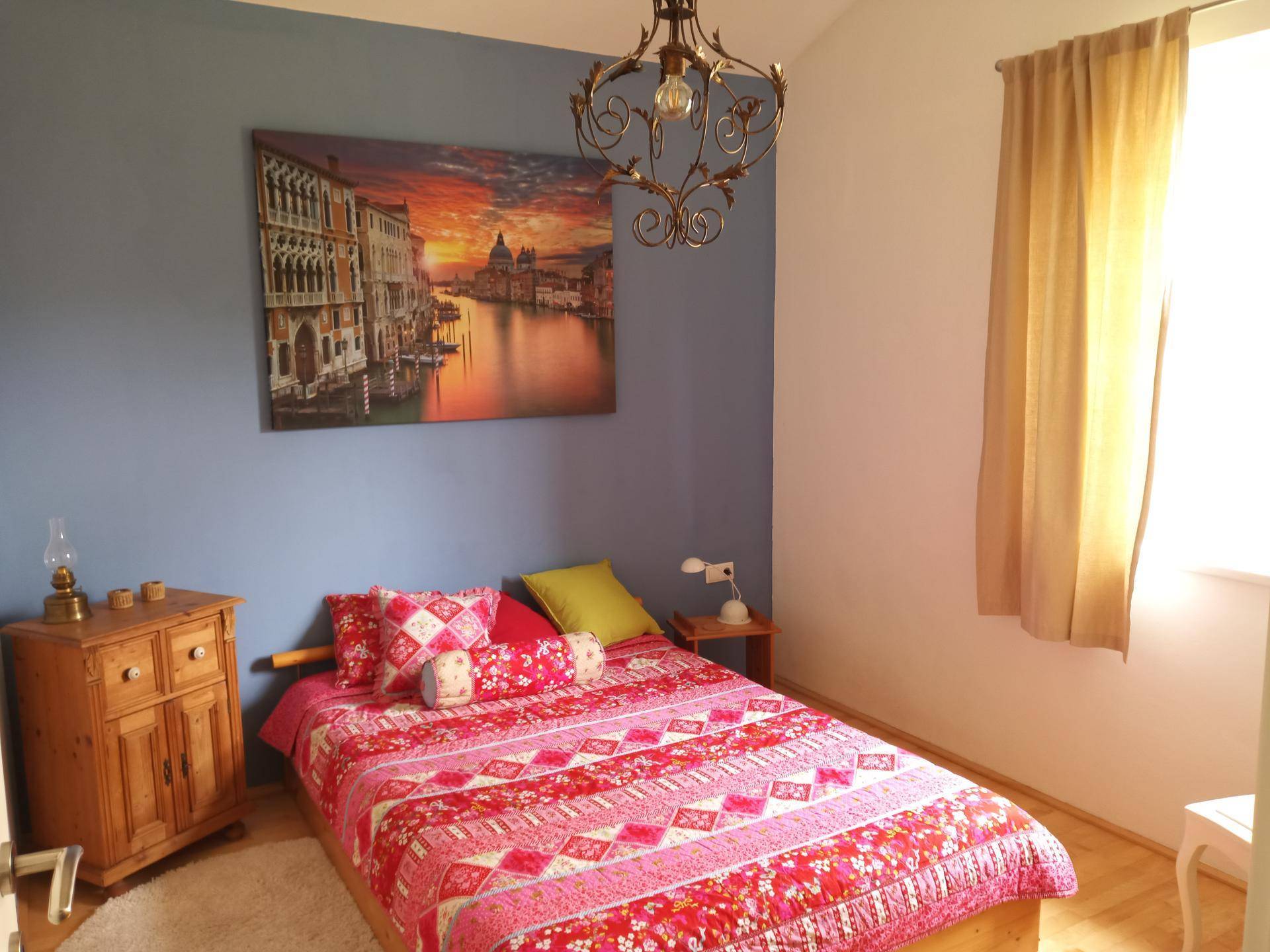 Schlafzimmer mit blauer Akzentwand, farbenfroher Bettwäsche und klassischem Kronleuchter.