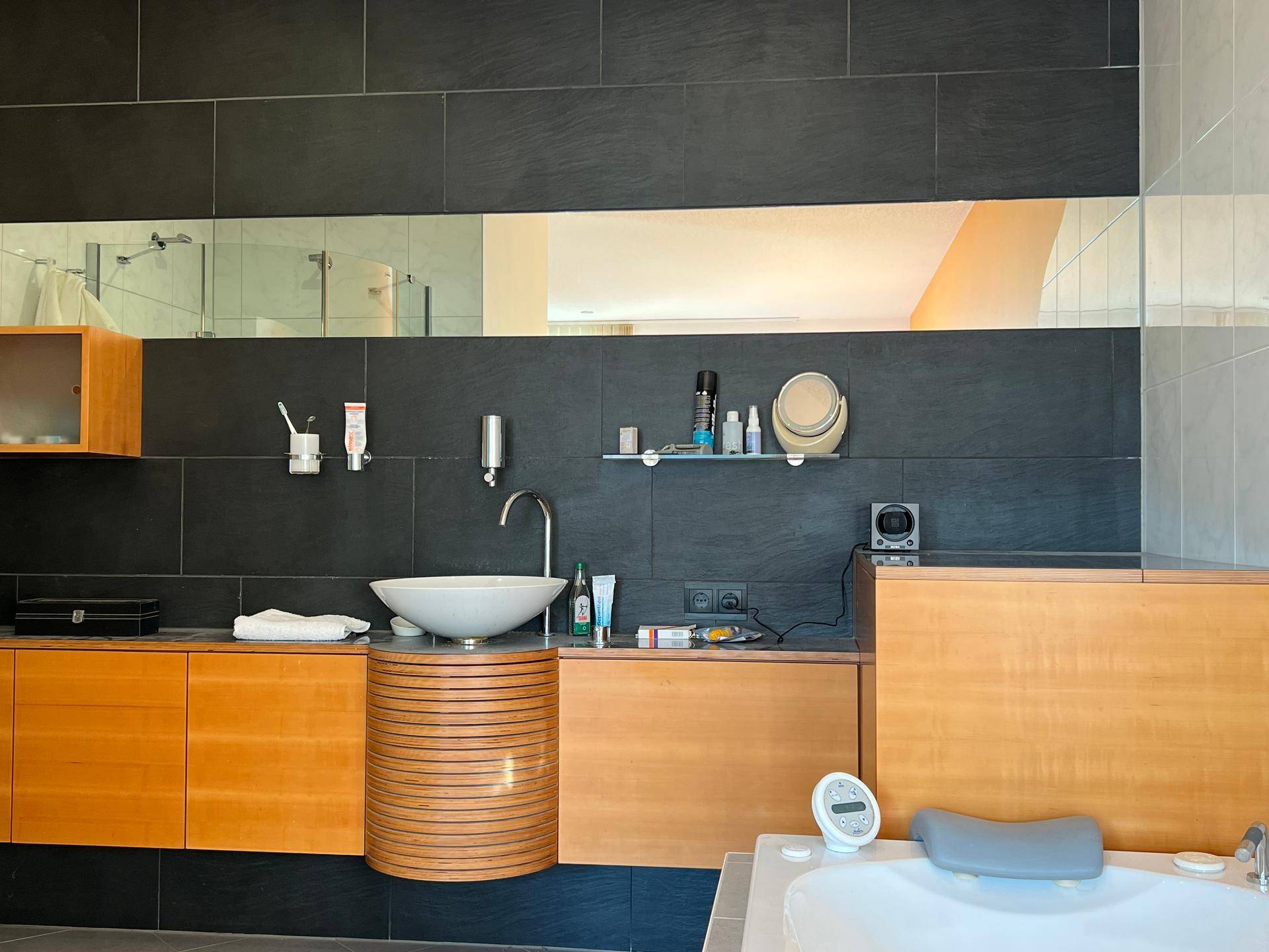 Modernes Badezimmer mit dunklen Fliesen, Holzmöbeln und einer integrierten Badewanne.