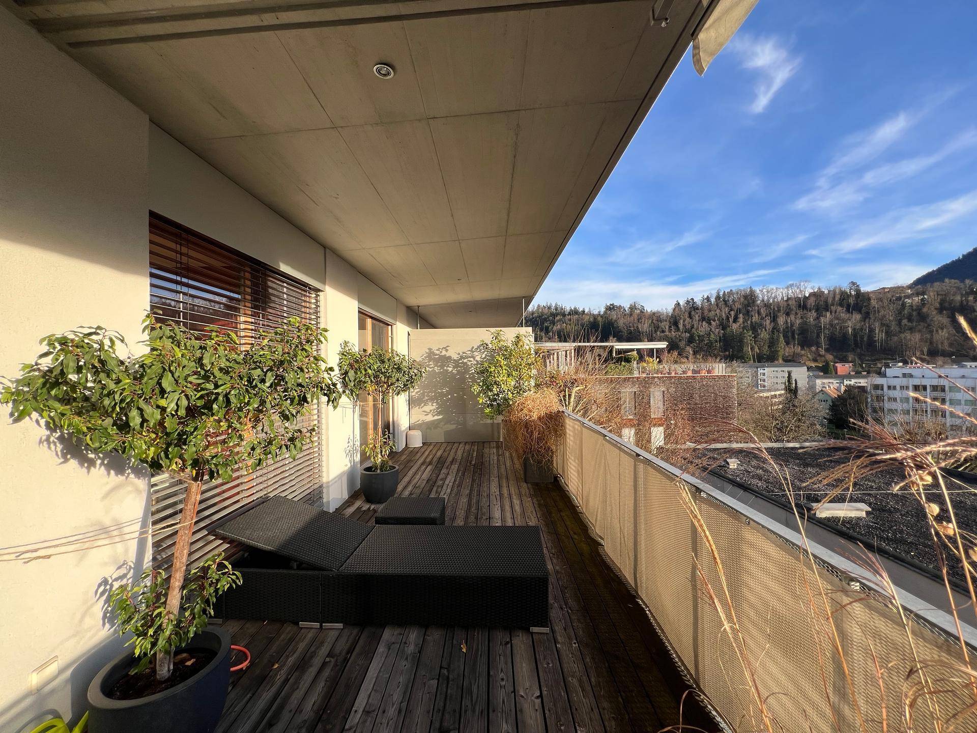 Großer Balkon mit Holzboden, Liegestühlen und Blick auf die grüne Umgebung.