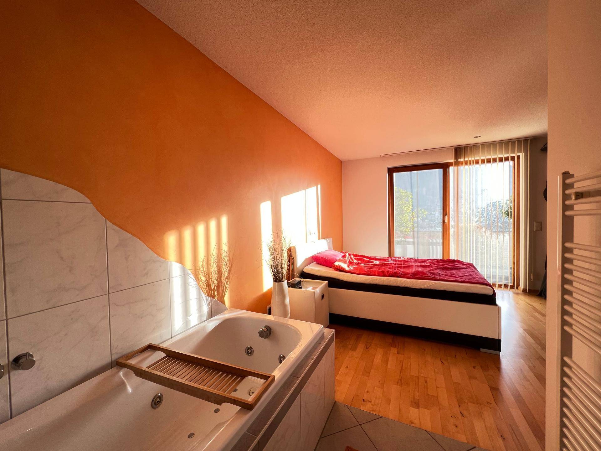 Geräumiges Schlafzimmer mit integrierter Badewanne, Holzboden und Zugang zum Balkon.