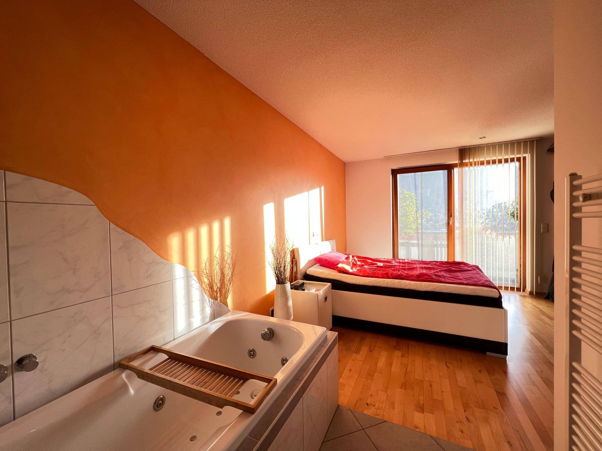 Geräumiges Schlafzimmer mit integrierter Badewanne, Holzboden und Zugang zum Balkon.