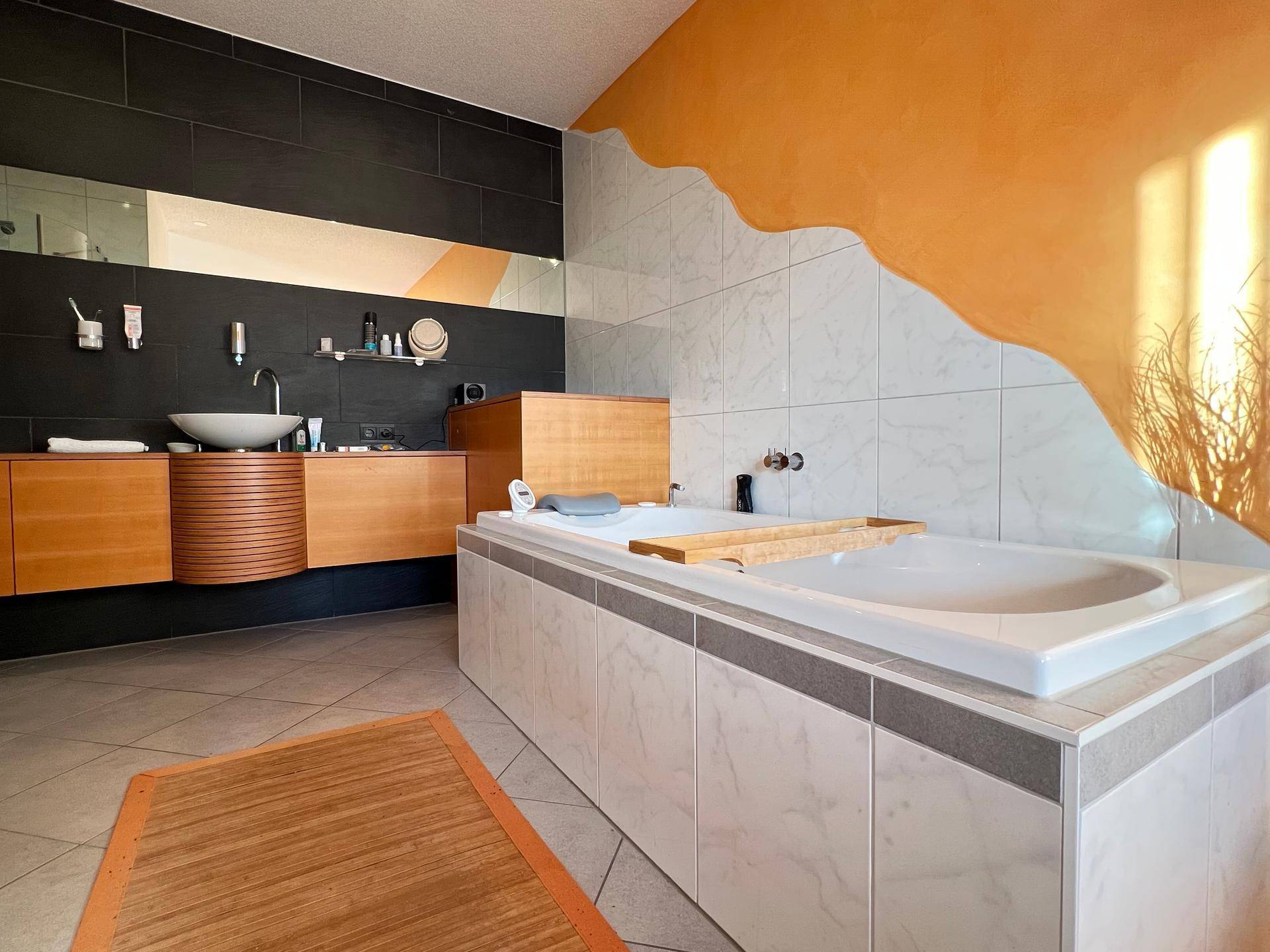 Modernes Badezimmer mit dunklen Fliesen, Holzmöbeln und einer großen Badewanne.