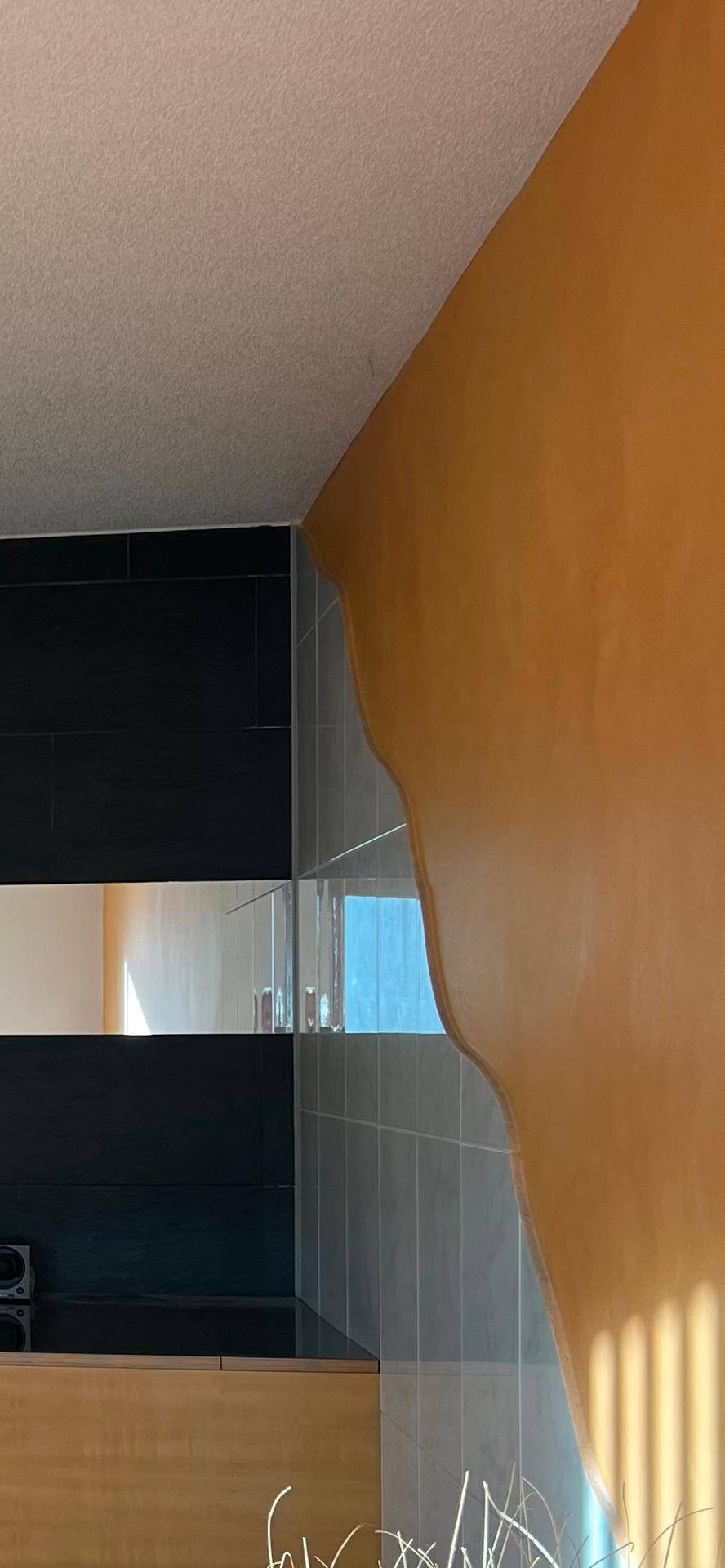 Detailansicht einer Wand mit Fliesen und orangefarbenem Putz, die verschiedene Bereiche verbindet.