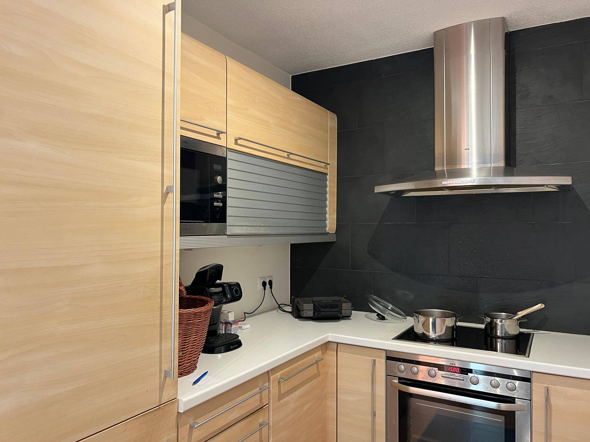 Moderne Küche mit hellen Holzschränken, integrierter Mikrowelle und Dunstabzugshaube.