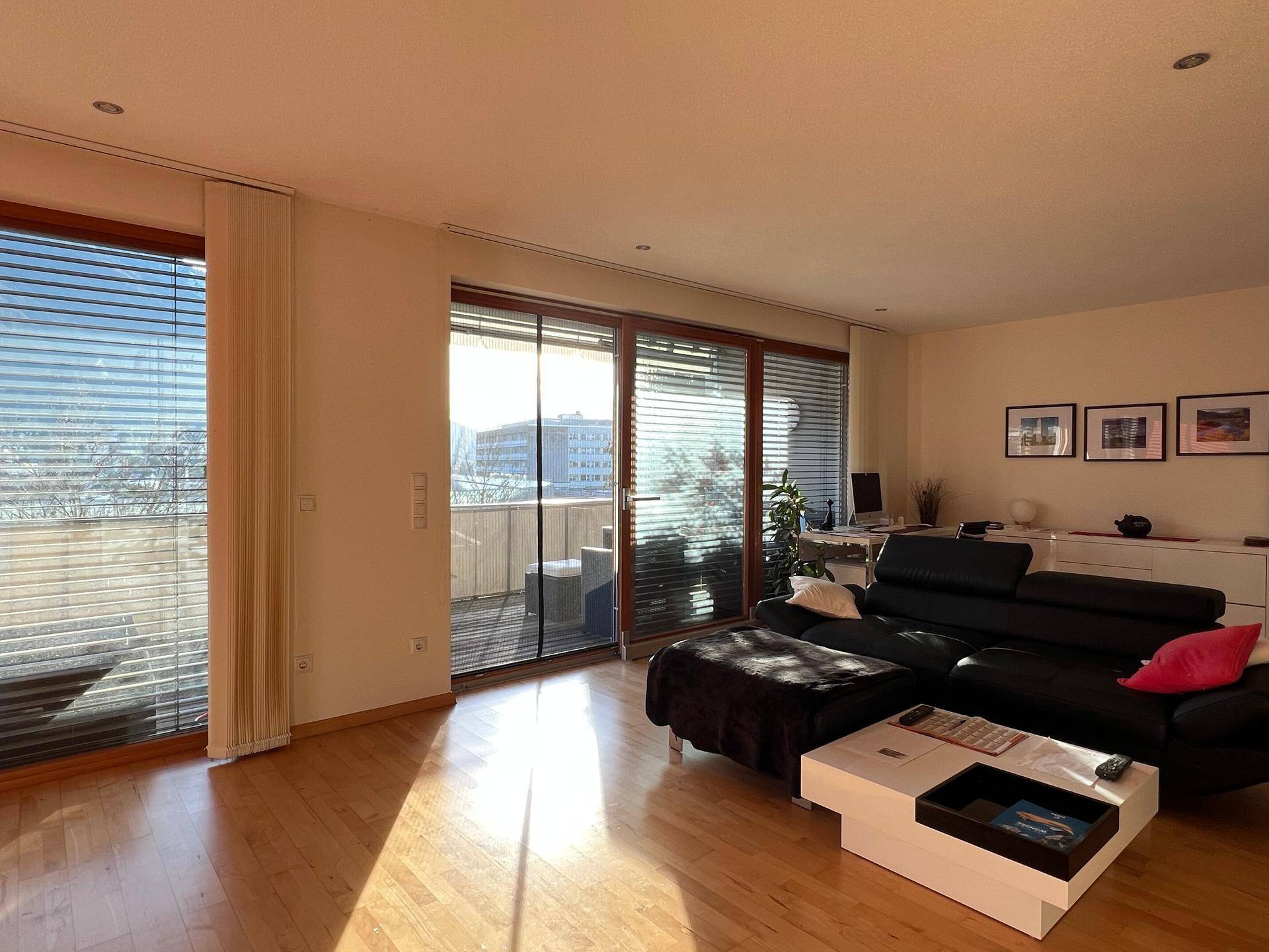 Heller Wohnbereich mit Holzboden, bequemer Couch und großen Fenstern mit Blick nach draußen.
