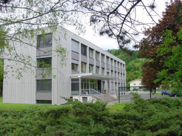 Modernes Bürogebäude mit klarer Architektur, umgeben von grüner Landschaft und Bäumen.