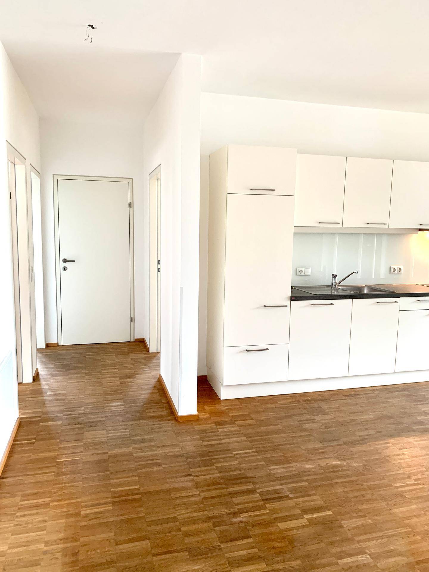 Heller Flur mit Parkettboden und Blick in die offene Küche des Apartments.