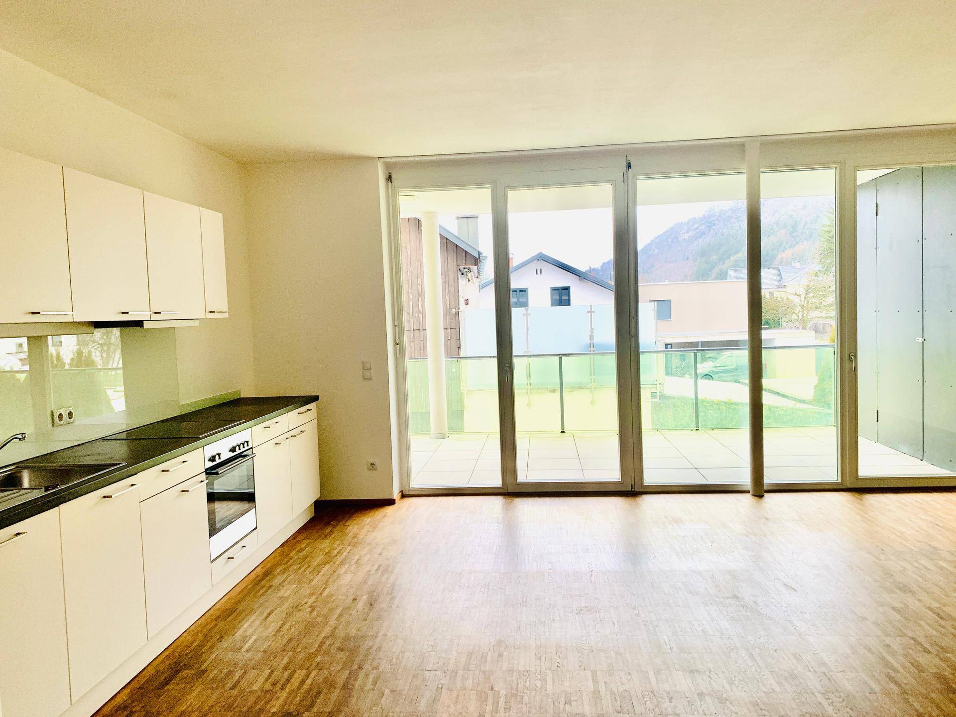 Helle offene Küche mit weißen Schränken, dunkler Arbeitsplatte und Zugang zum Balkon.